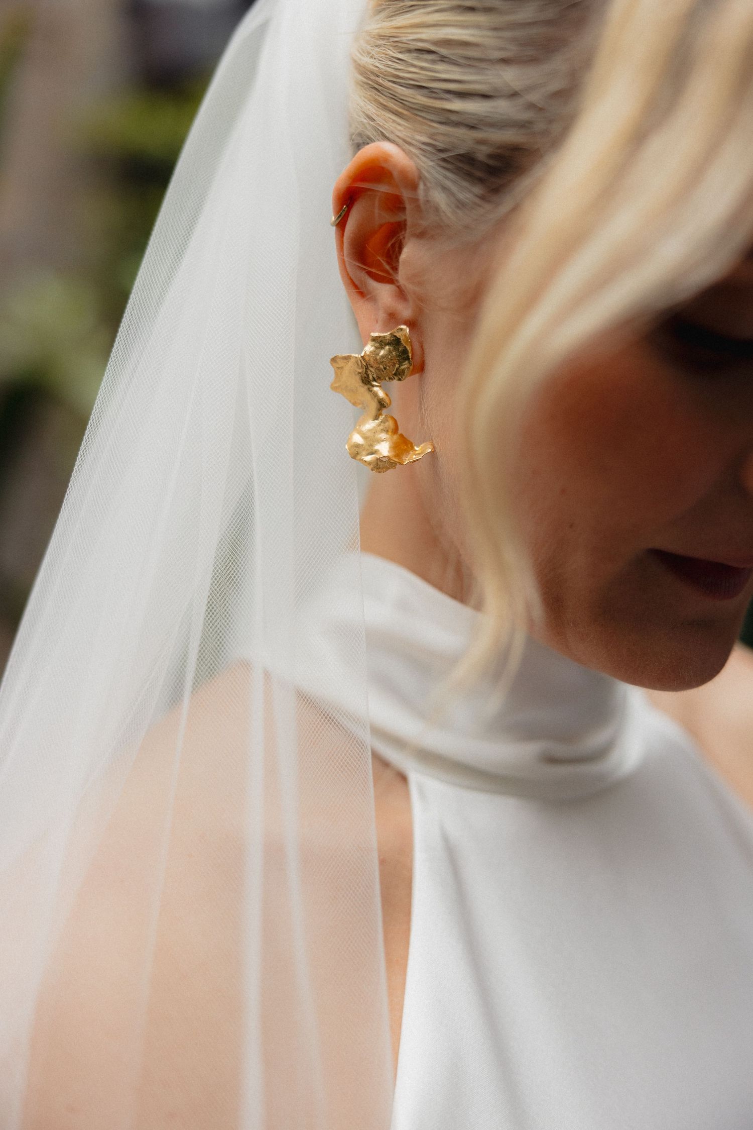 Close-up of a bride wearing an elegant gold statement earring with her white veil.
