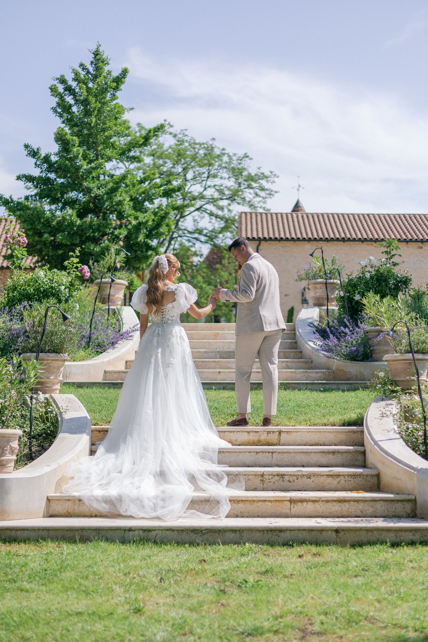 A wedding couple poses on stone steps in an outdoor garden setting.