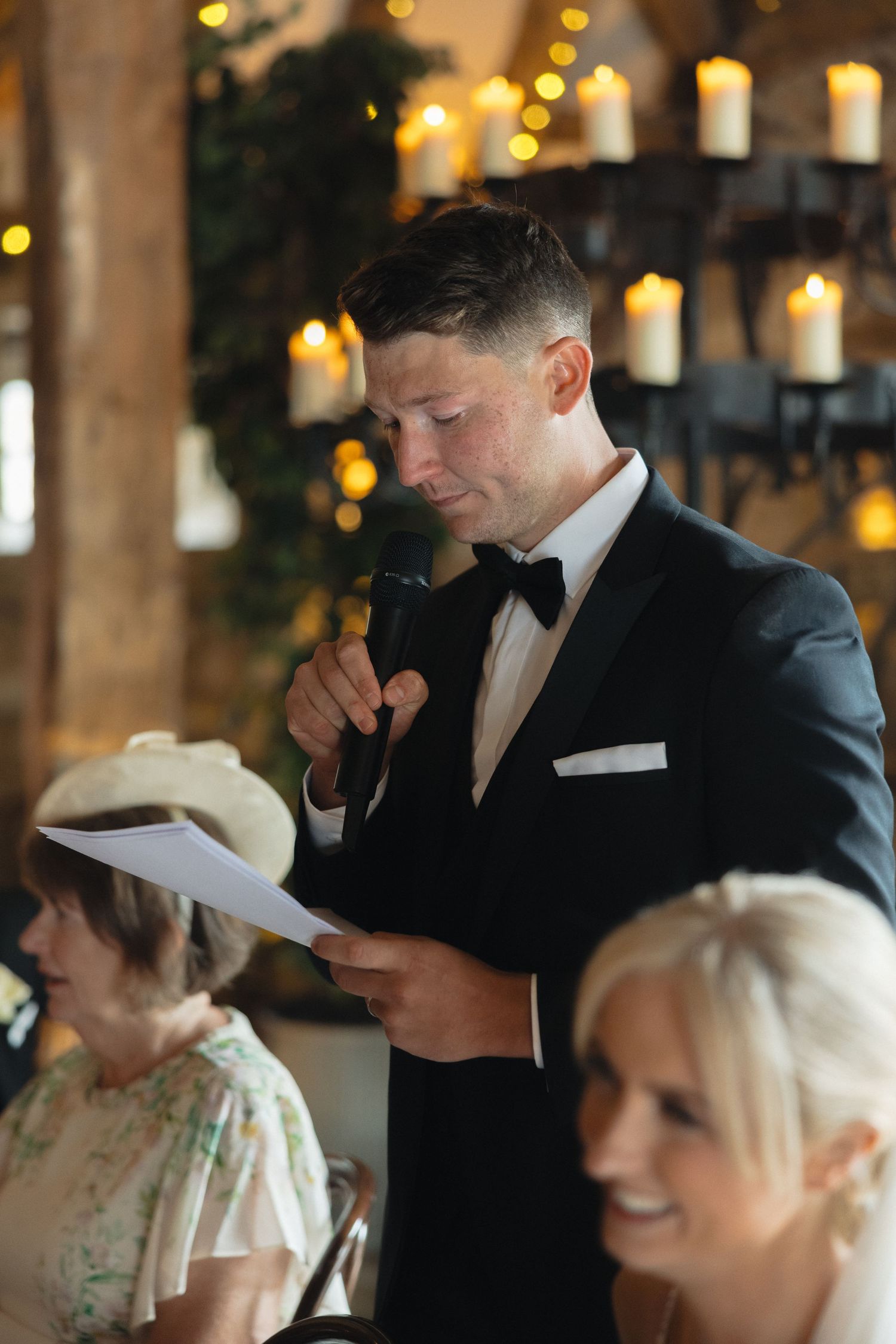 Wedding guests share smiles during speeches at an elegant indoor reception.