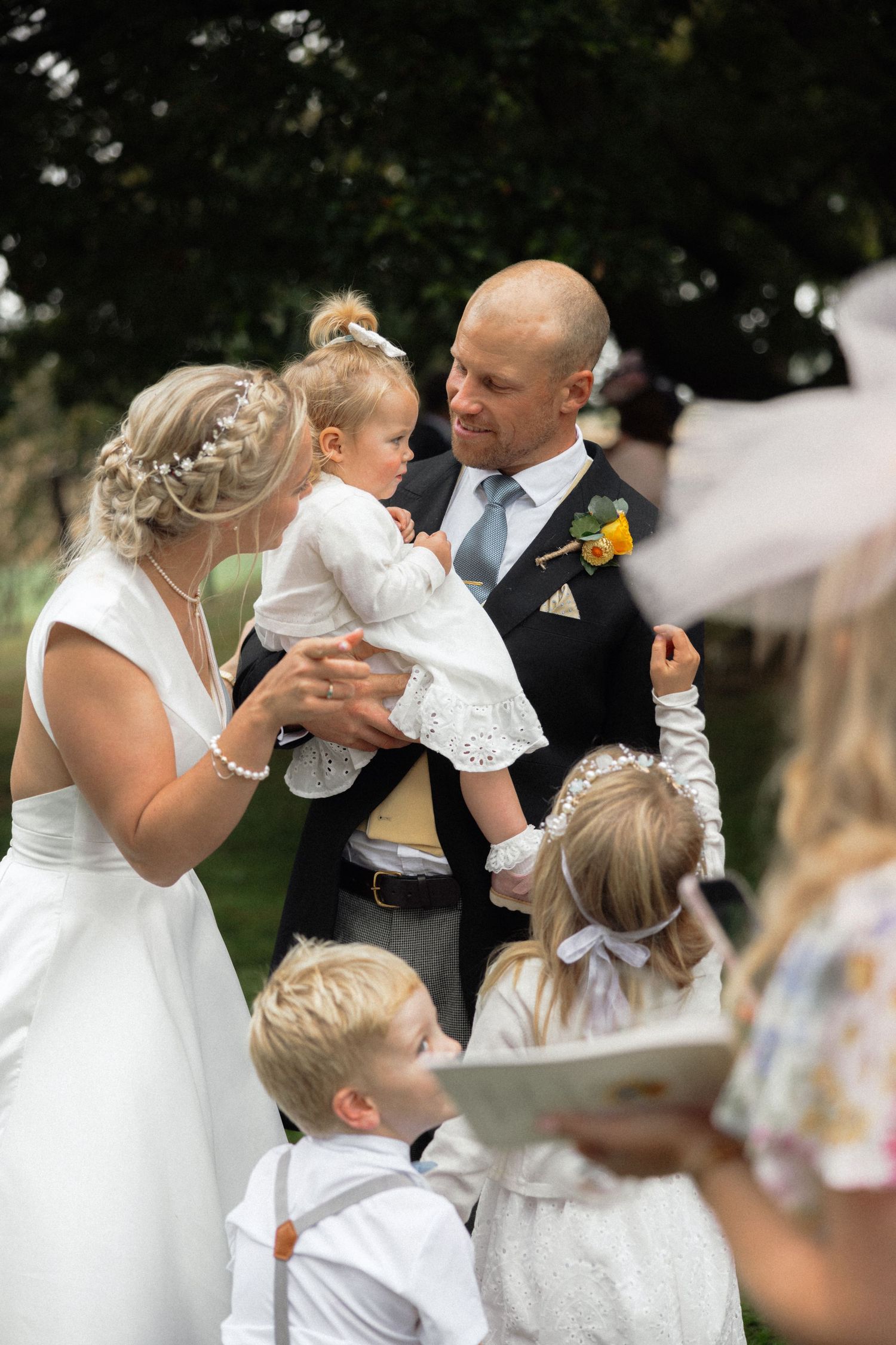 Wedding party gathering with children in white formal attire during outdoor celebration.