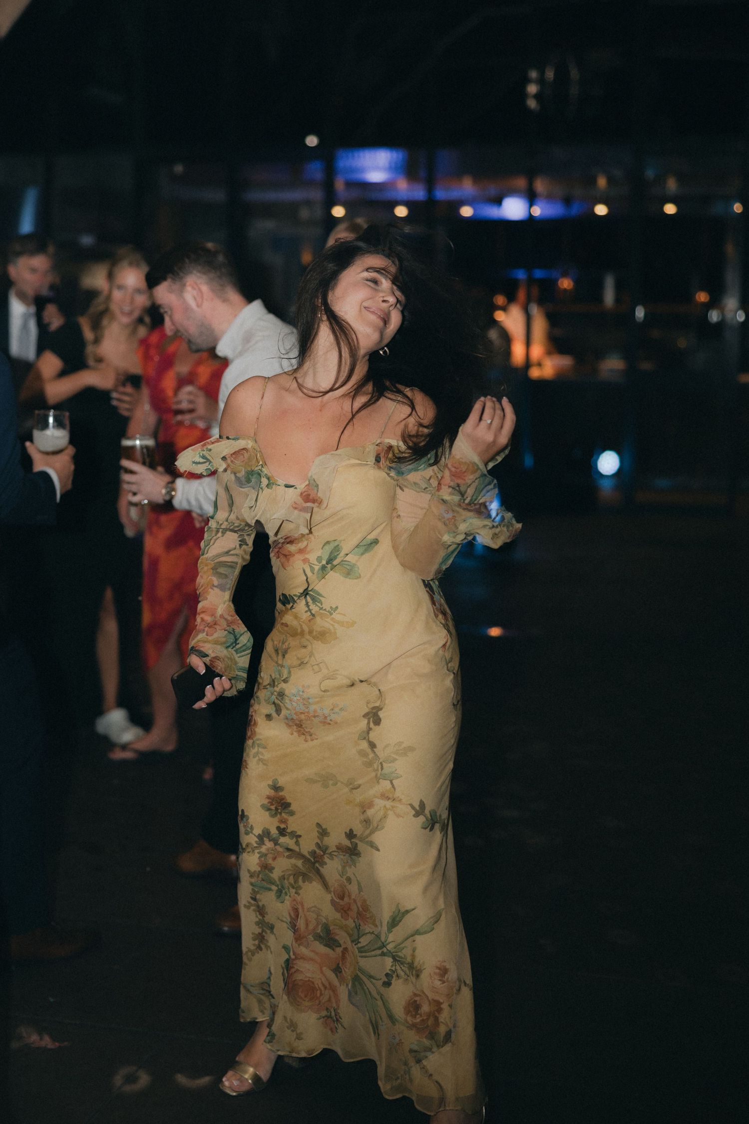Woman in floral yellow dress dances joyfully at evening reception.