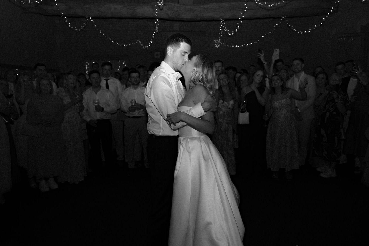 Black and white shot of couple's first dance surrounded by wedding guests.