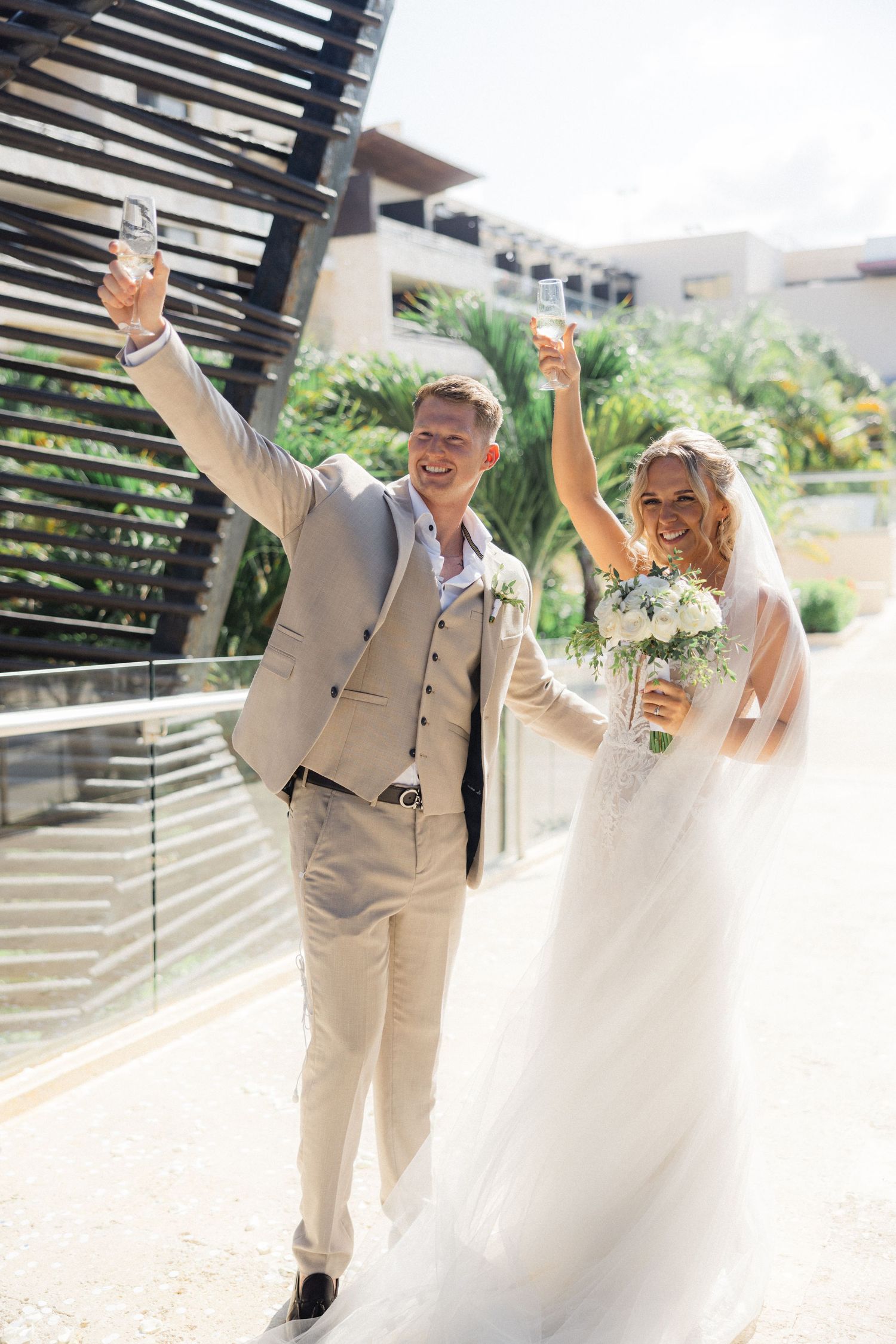 Joyful couple celebrates walking down pathway at tropical beach wedding venue.