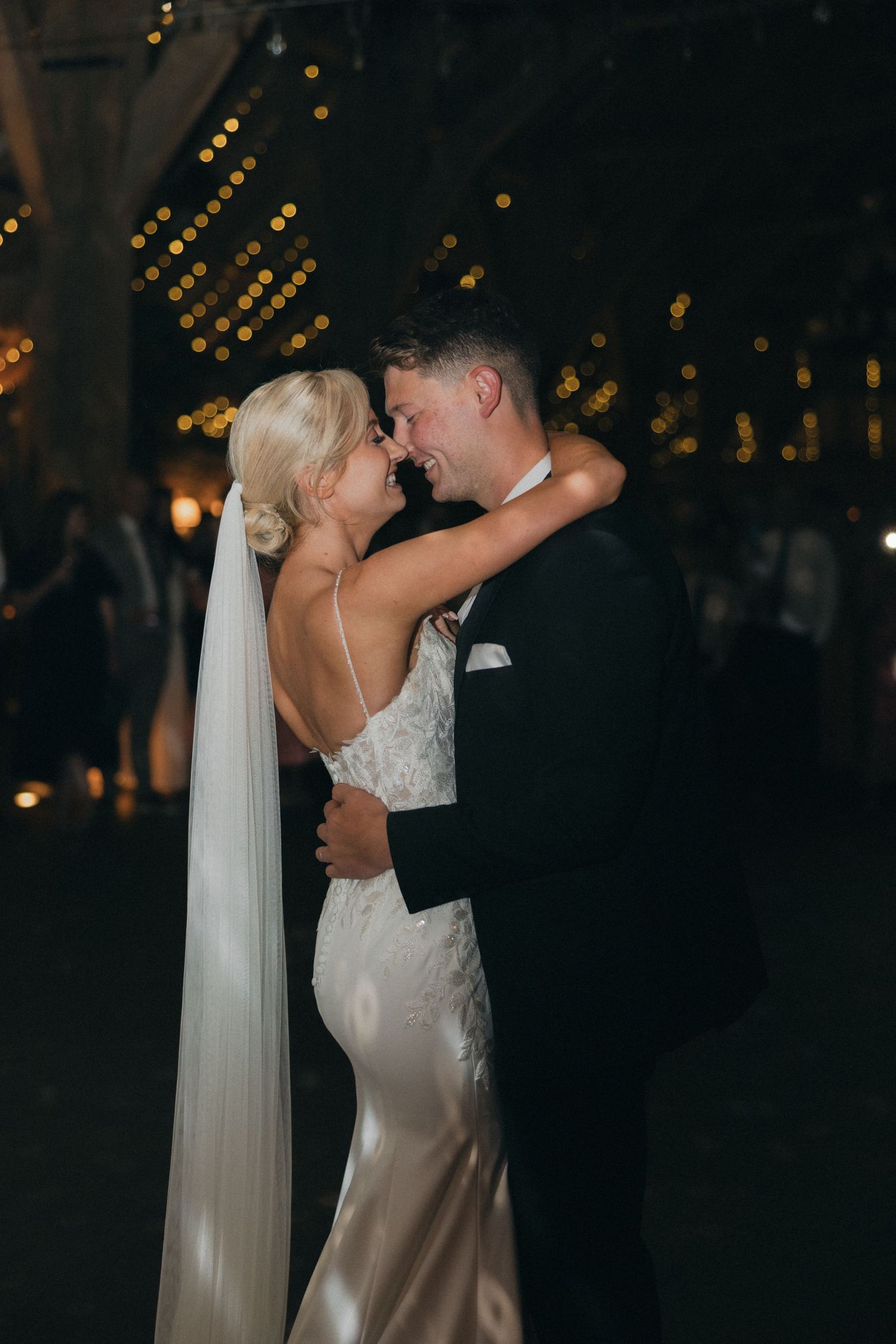 An intimate moment between newlyweds during their first dance with twinkling lights in the background.