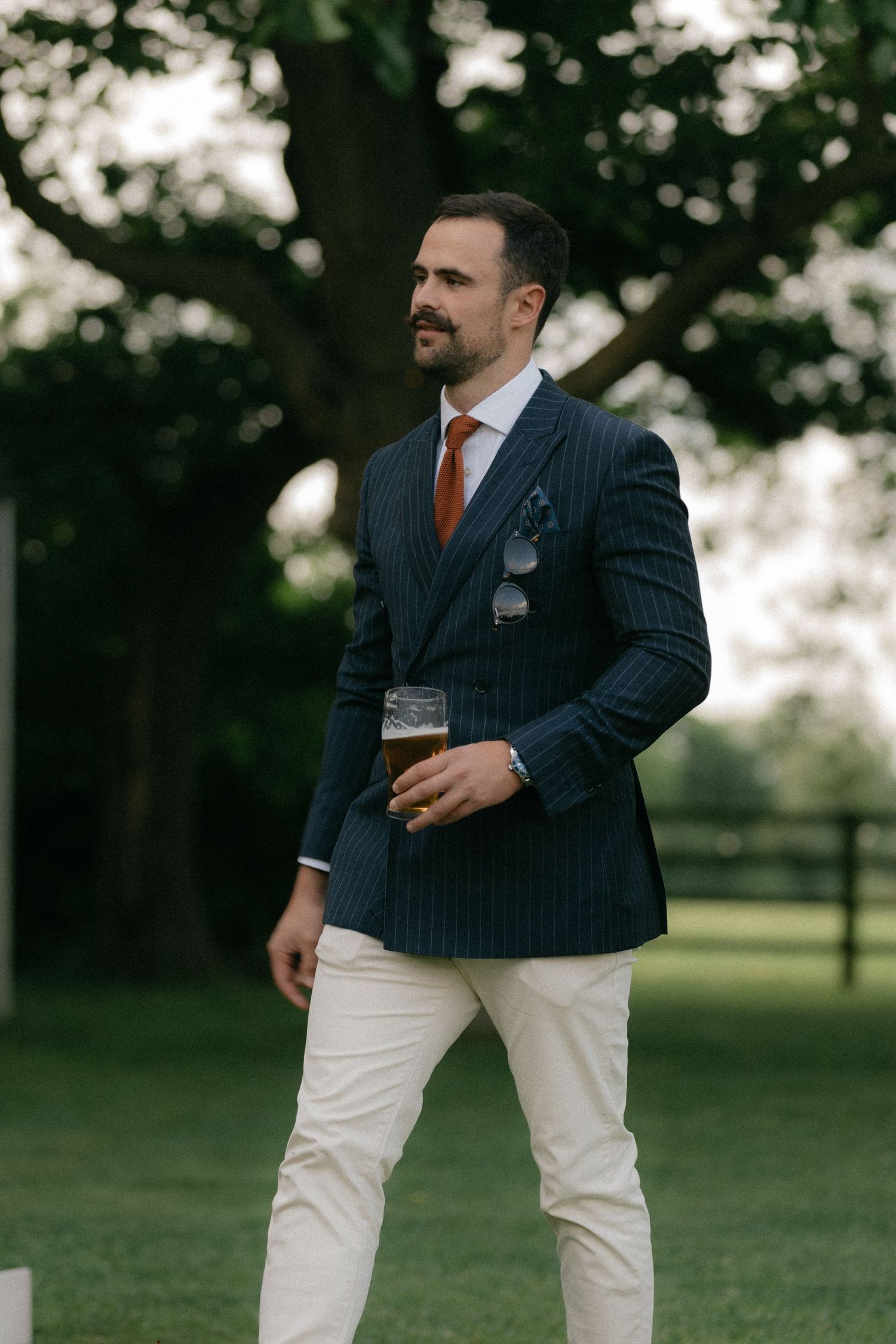 Groomsmen in pinstripe suits and white pants socialize at an outdoor wedding.