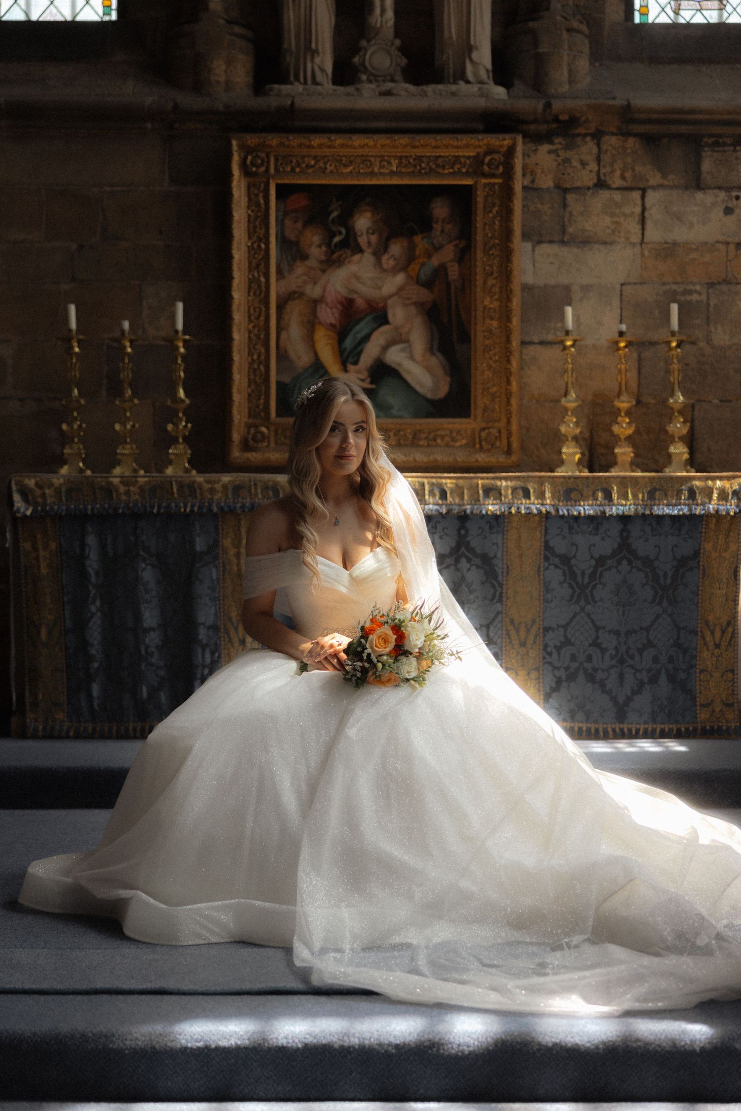A bride in a flowing white gown poses dramatically in a church setting with dramatic lighting.