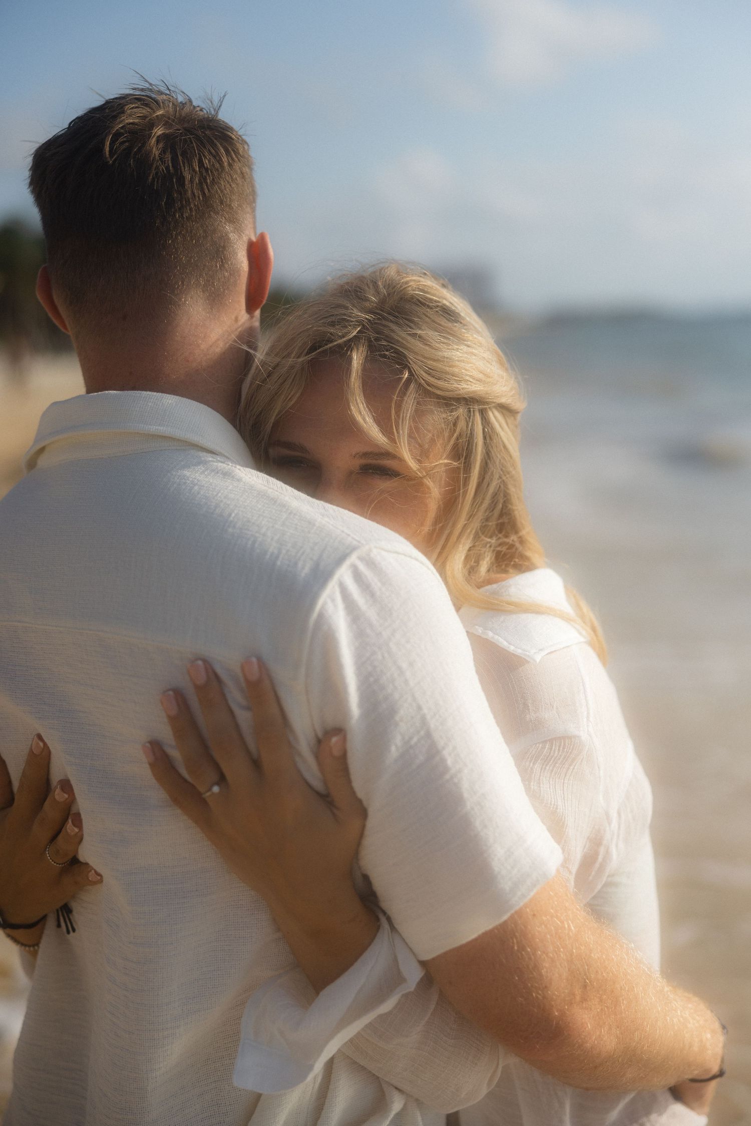A romantic embrace captured on a sunny beach with ocean waves in the background.