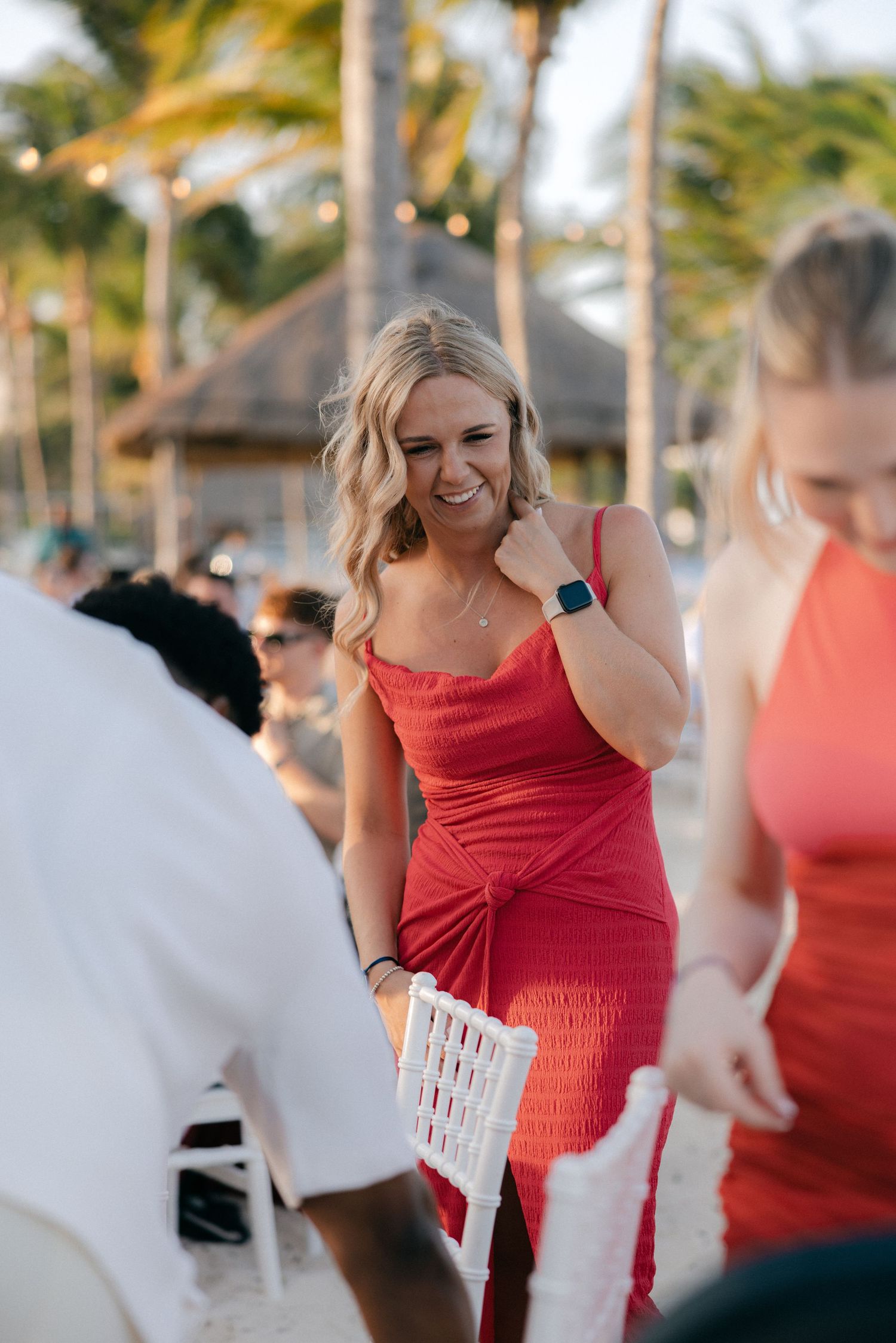 Guest in red dress holding paper at outdoor tropical venue.