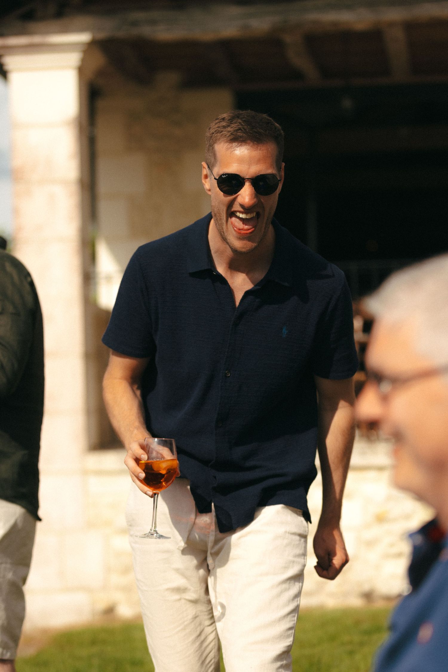 Person in navy polo and sunglasses enjoying a drink outdoors on a sunny day.
