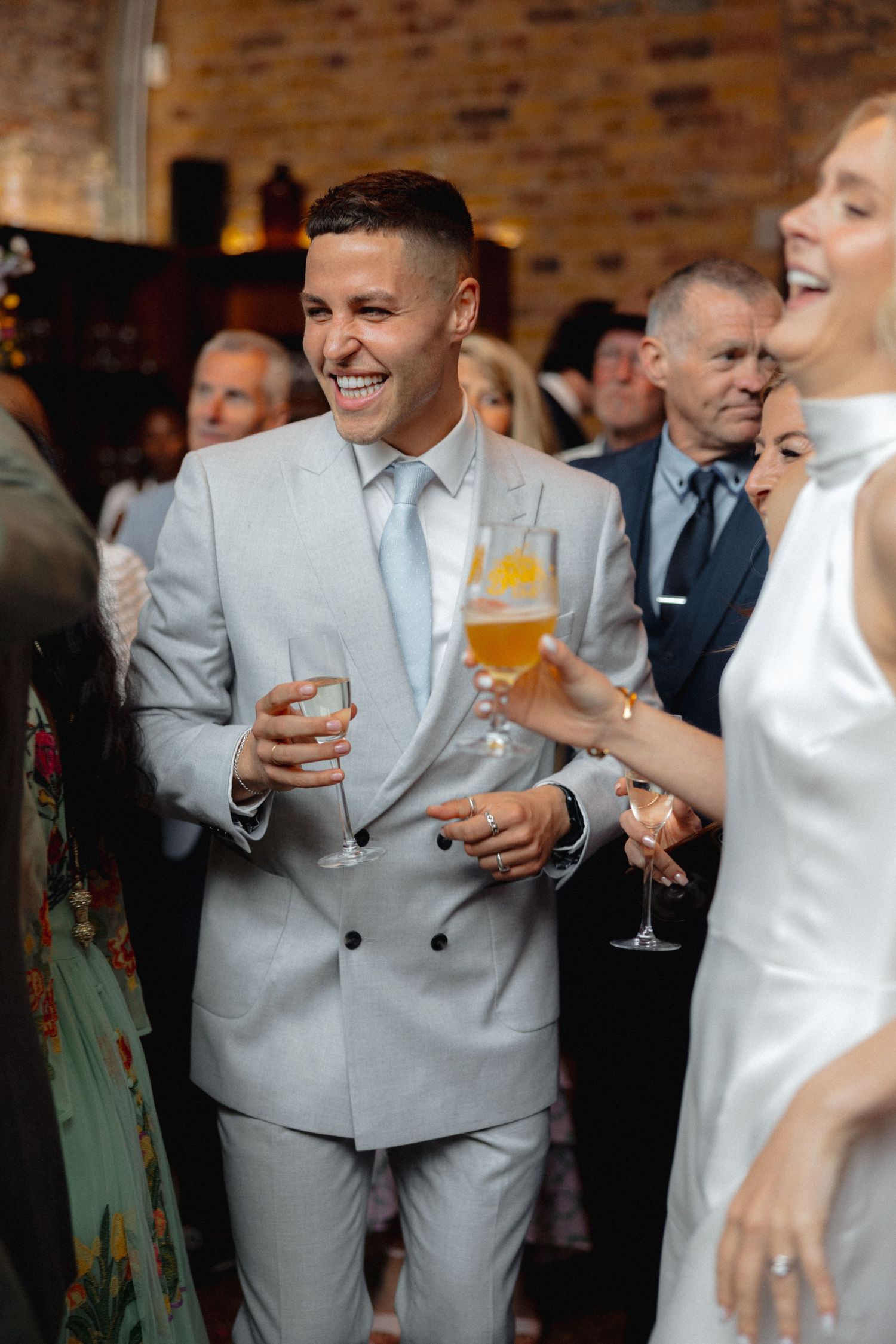 Wedding celebration with guests laughing and holding champagne glasses in an industrial-style venue.