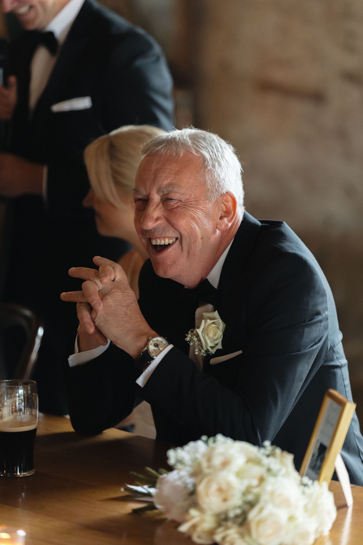 Guests share emotional laughter during wedding speeches at an elegantly set dinner table.
