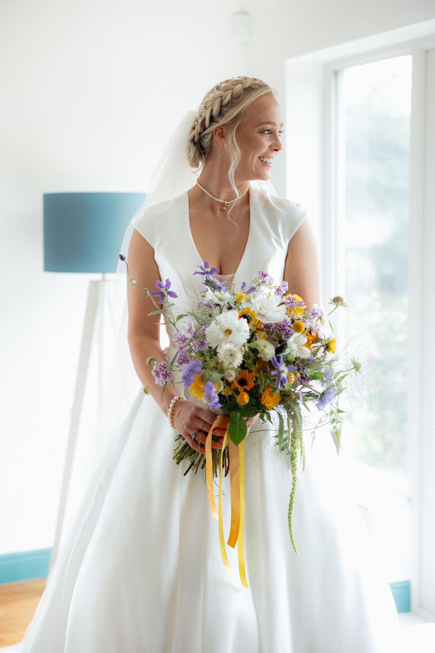 Wedding bouquet with colorful wildflowers and yellow ribbons against white dress.