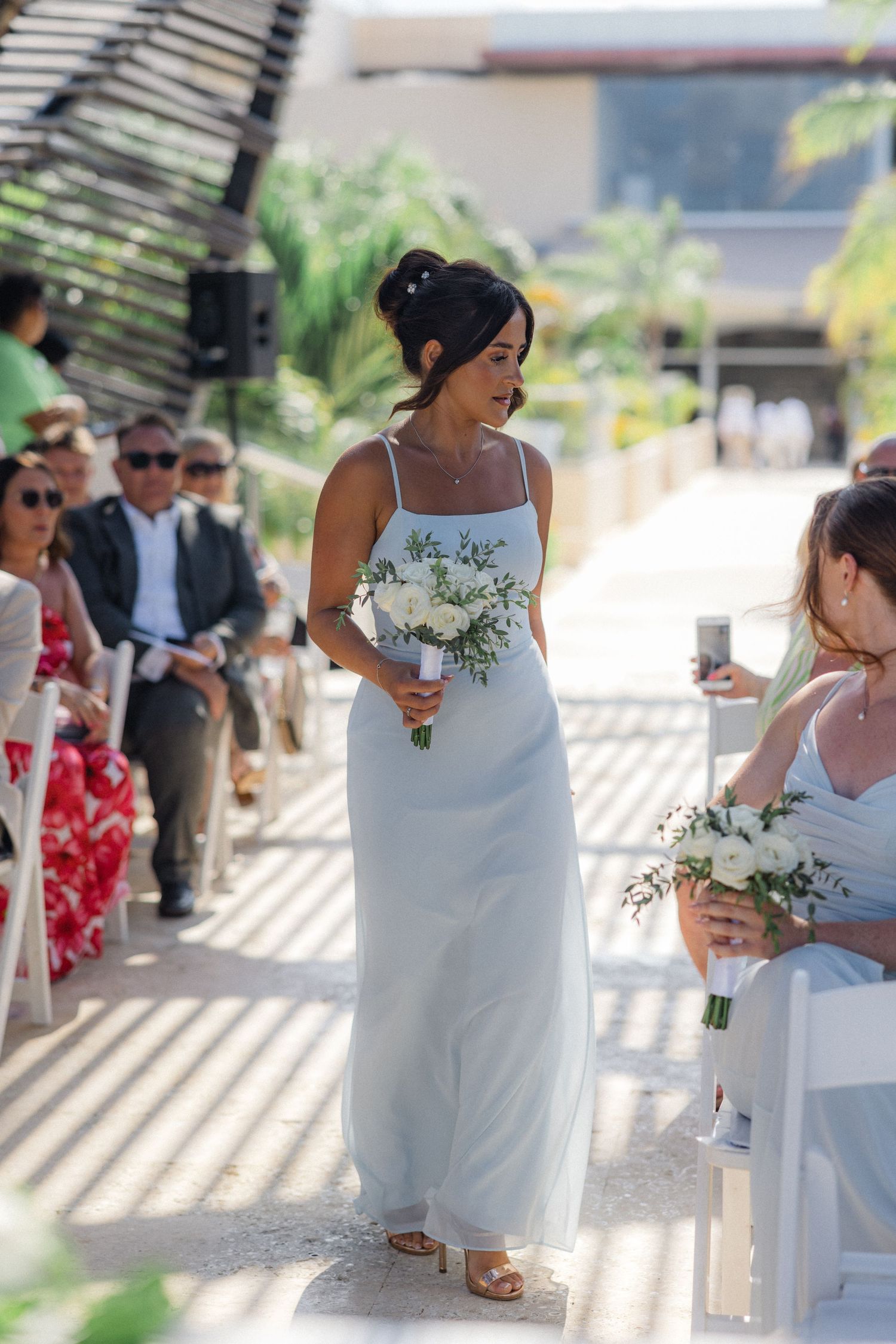 Wedding ceremony processional with attendants walking down an aisle under geometric shadows.