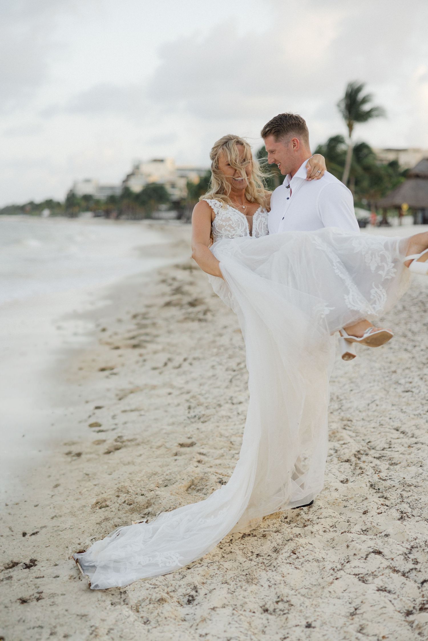 Wedding couple frolics on beach as bride's white dress flows dramatically in the wind.