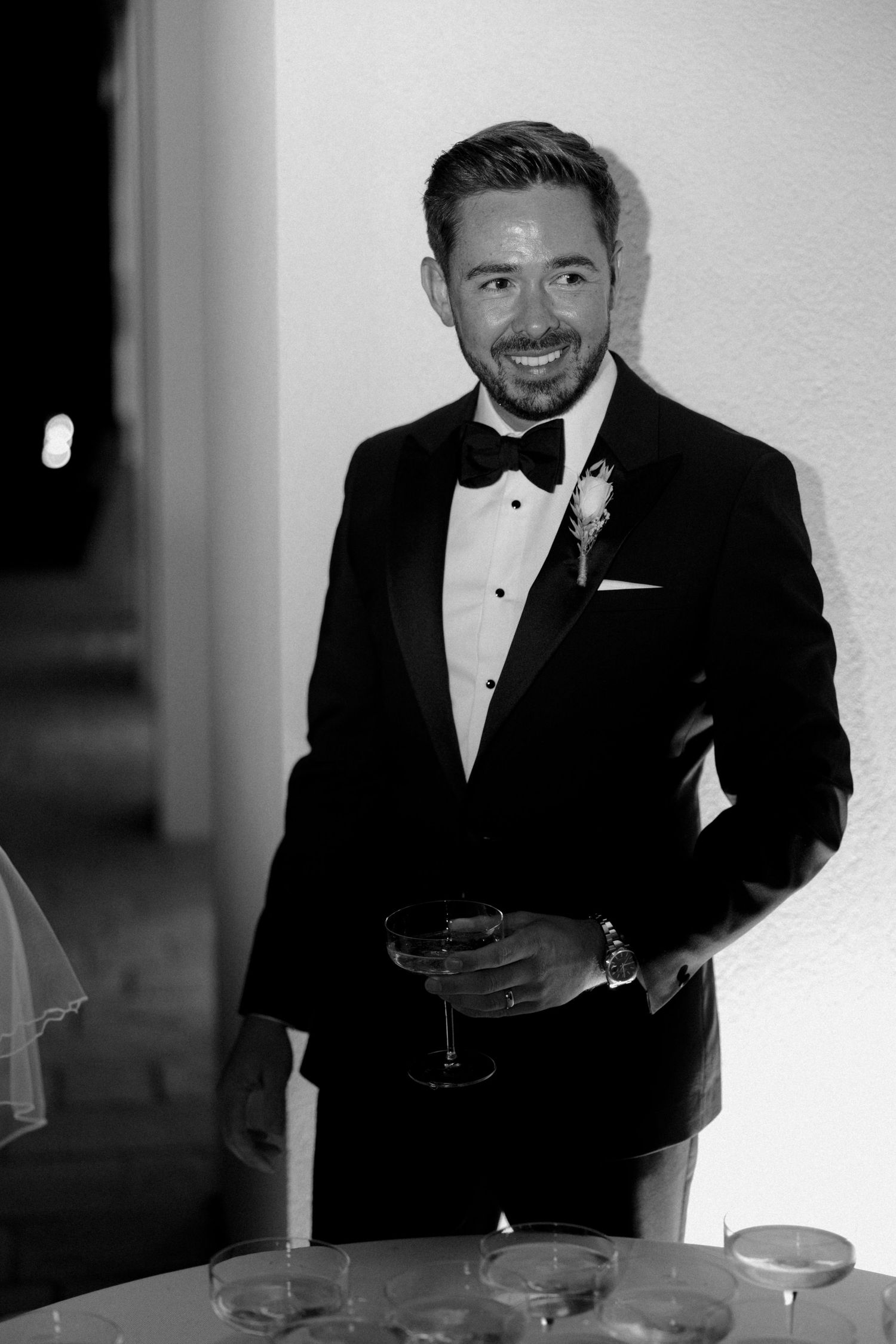 Person in tuxedo smiling while standing next to champagne tower setup.