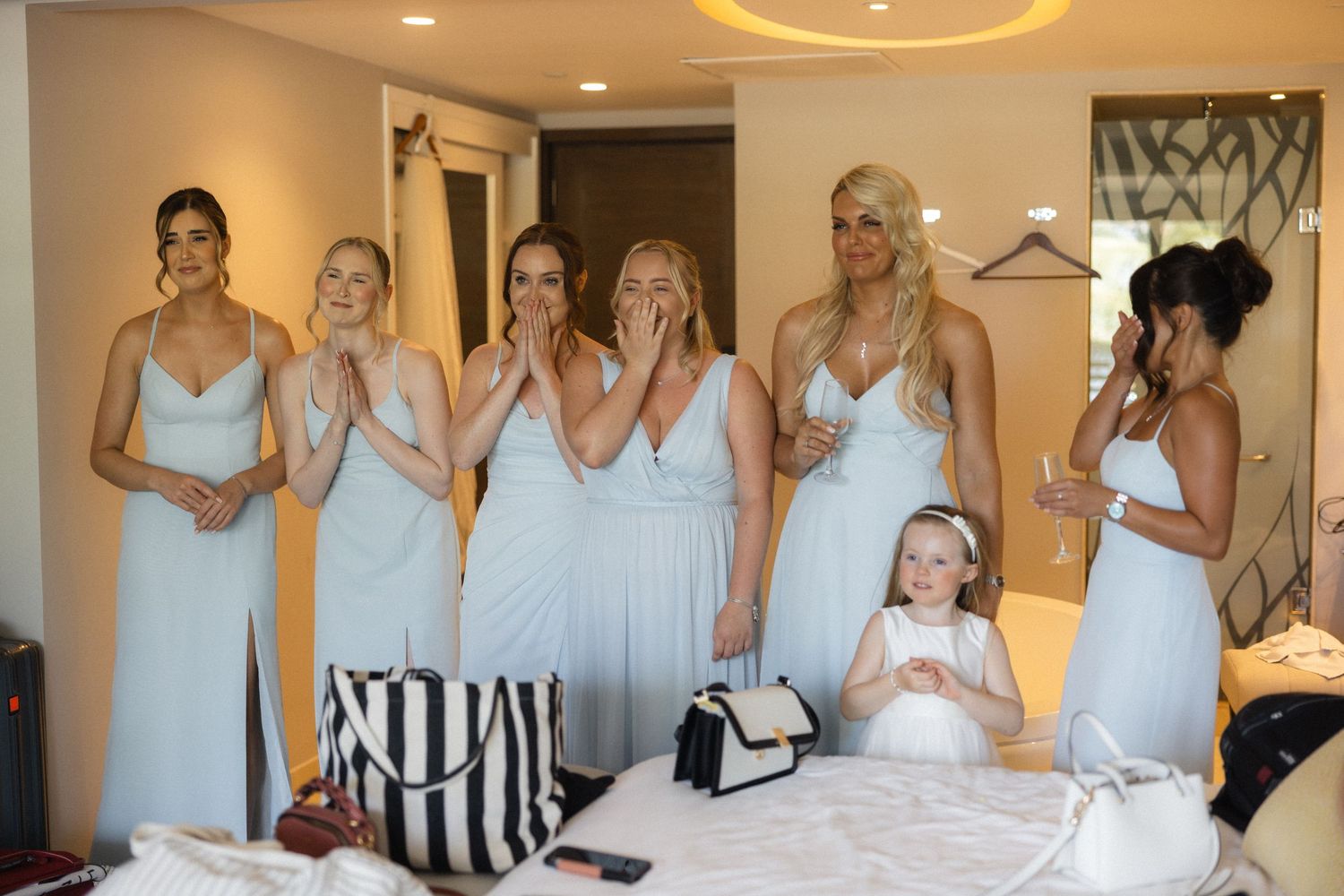 Wedding party in matching light blue dresses reacting with joy during preparations.