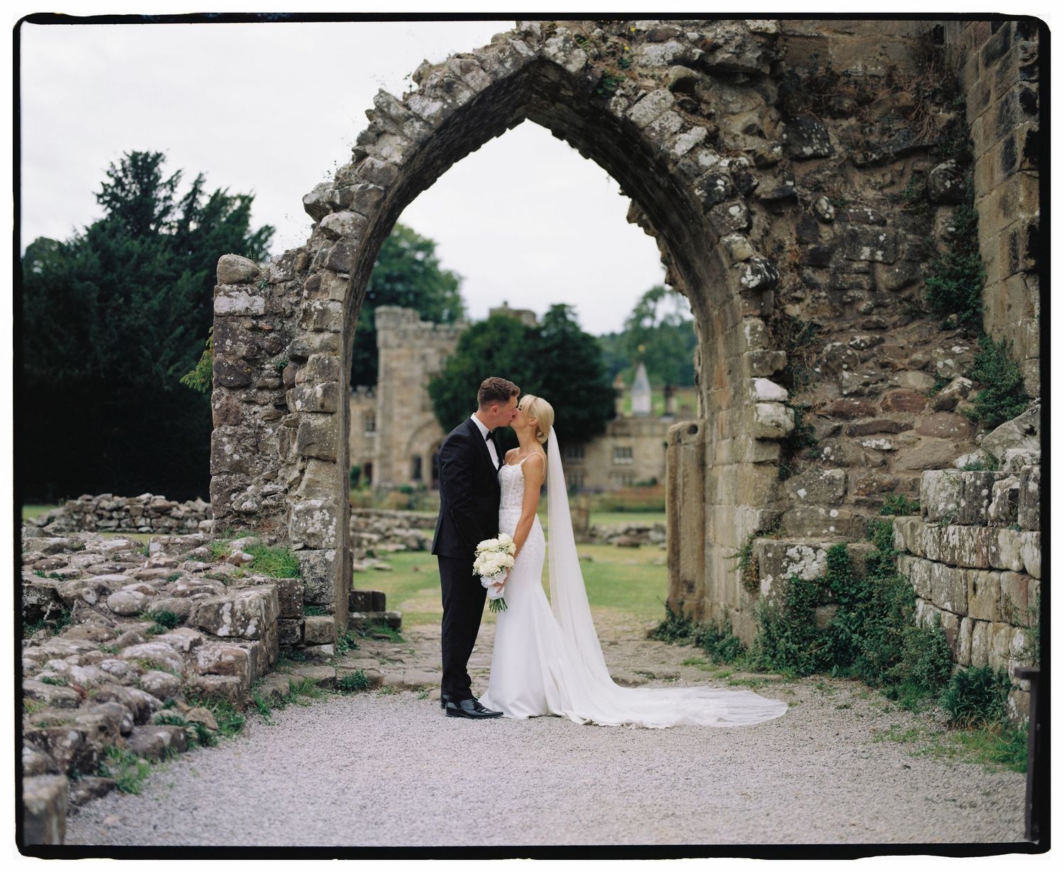 A romantic wedding portrait under a historic stone arch in ruins.