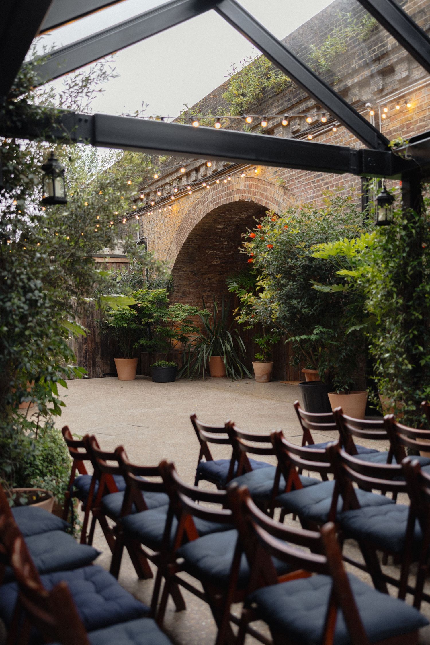 Indoor wedding venue with rows of wooden chairs and string lights under brick archways.