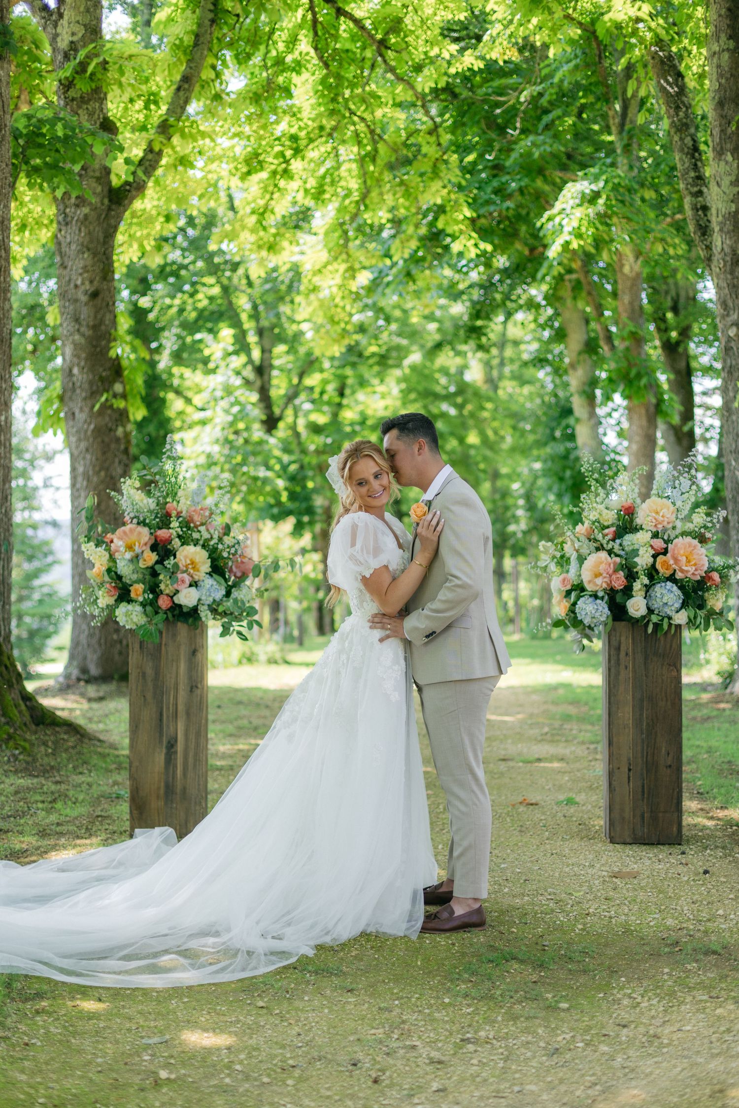 A wedding couple shares a moment among trees decorated with floral arrangements.