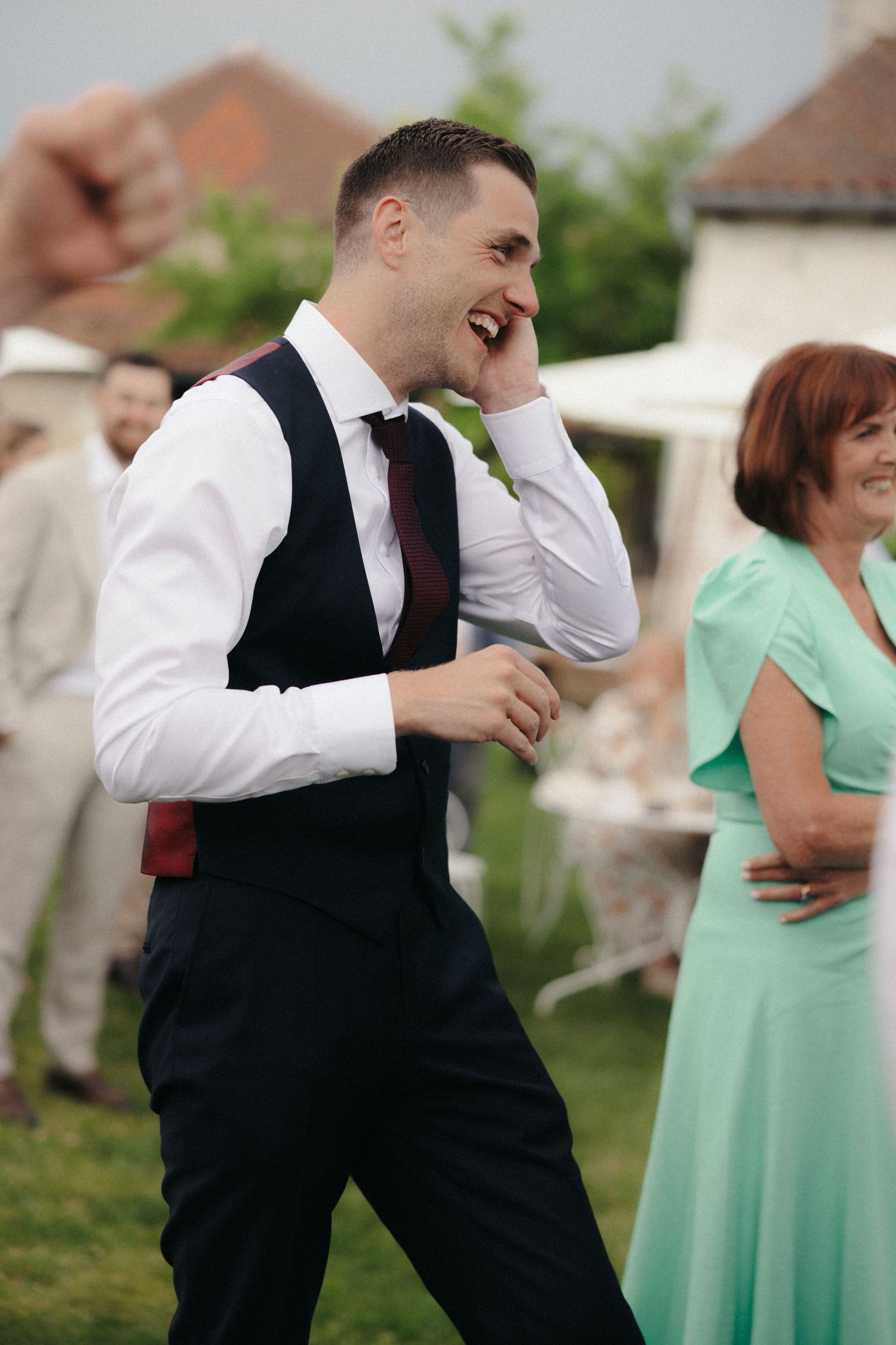 Wedding party members in mint green dresses and black vests dance joyfully at an outdoor reception.