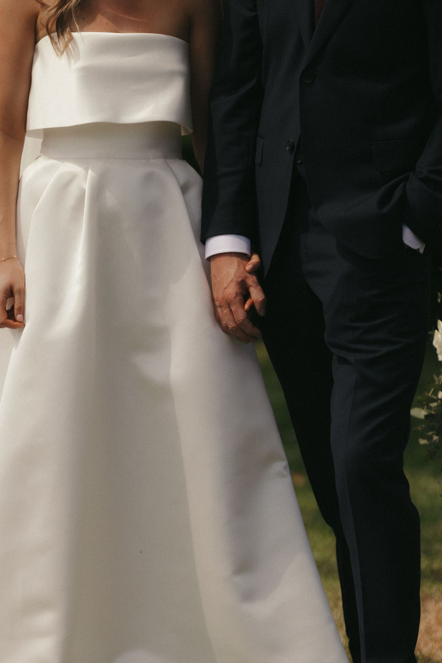 Close-up detail of a white wedding dress and black tuxedo as couple stands together.