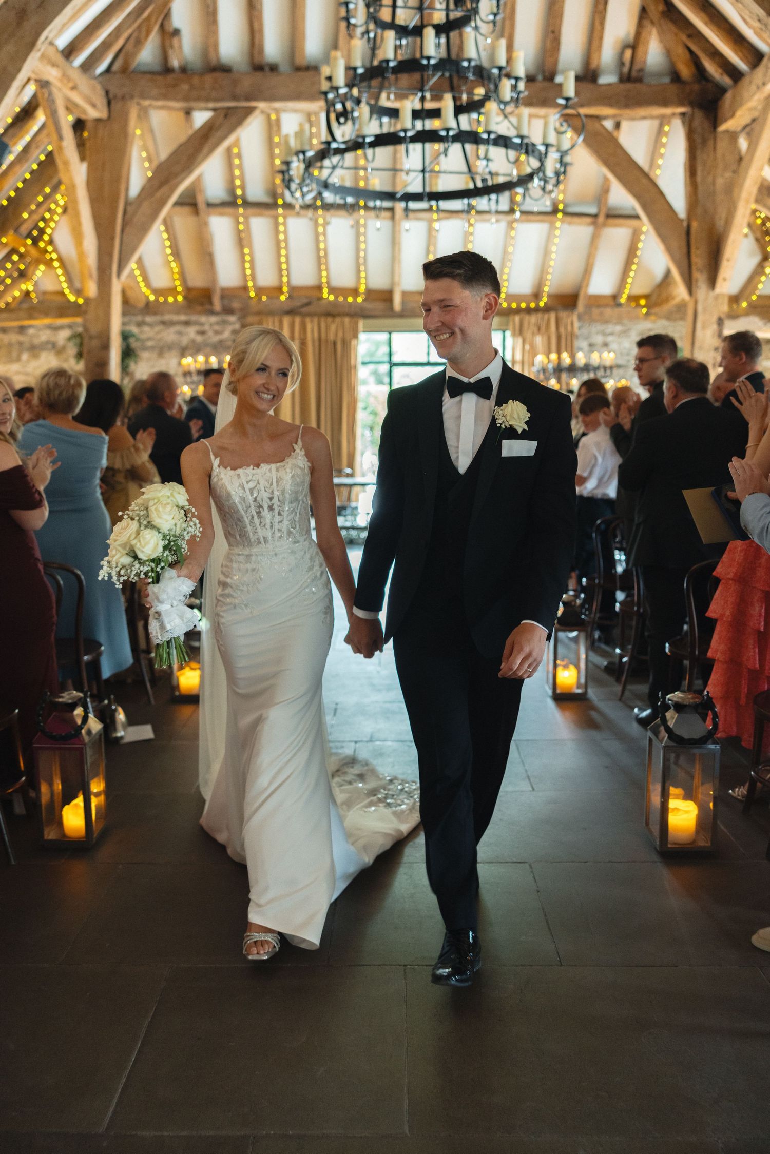 Wedding celebration in rustic barn venue with chandelier lighting and wooden beam architecture.