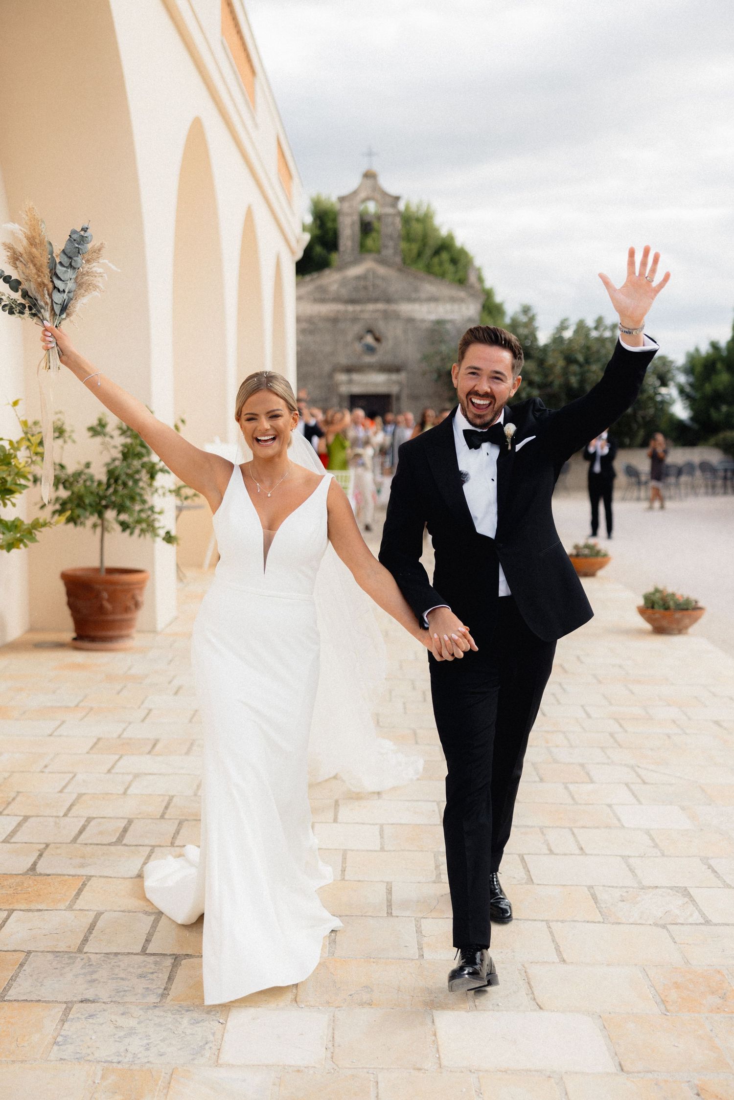 Playful wedding party poses on a stone patio with dramatic gestures.