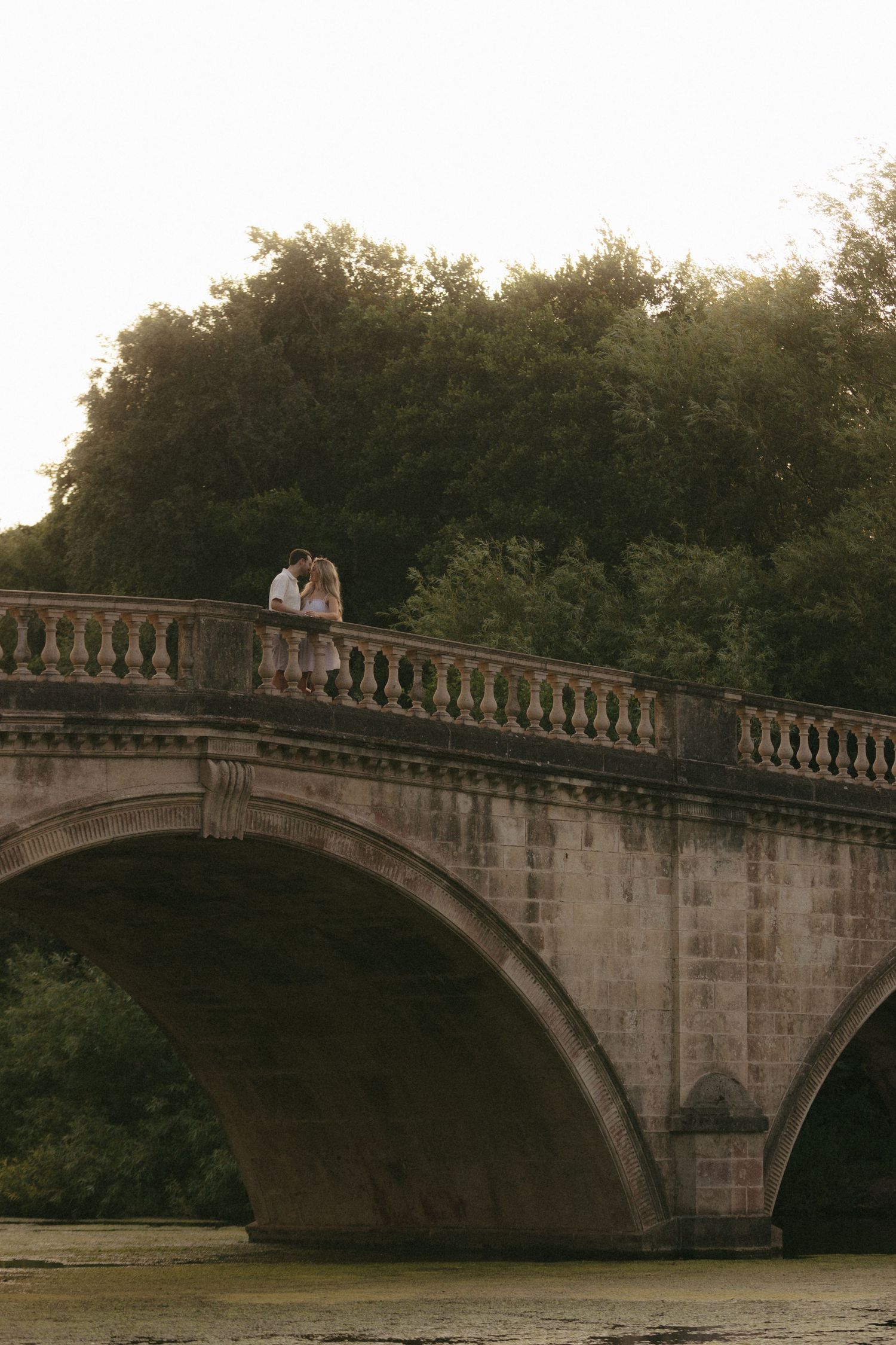 A couple stands on a historic stone bridge at sunset creating a romantic silhouette.