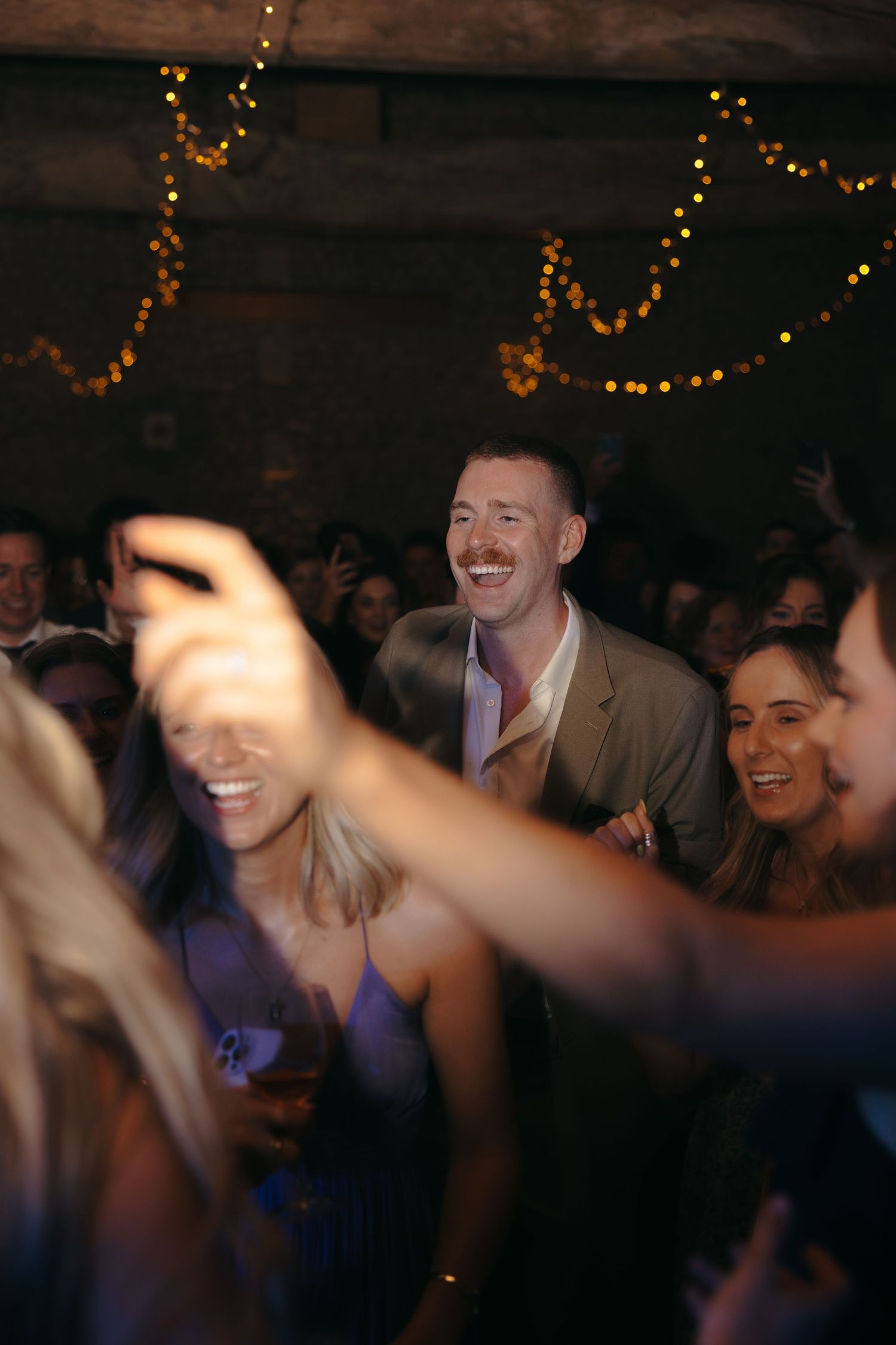 Wedding reception guests dancing and laughing under string lights.