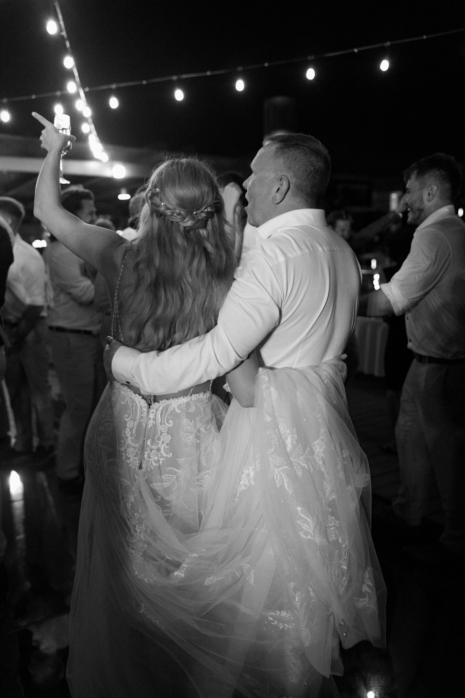 Wedding couple dances together under string lights during their evening reception celebration.
