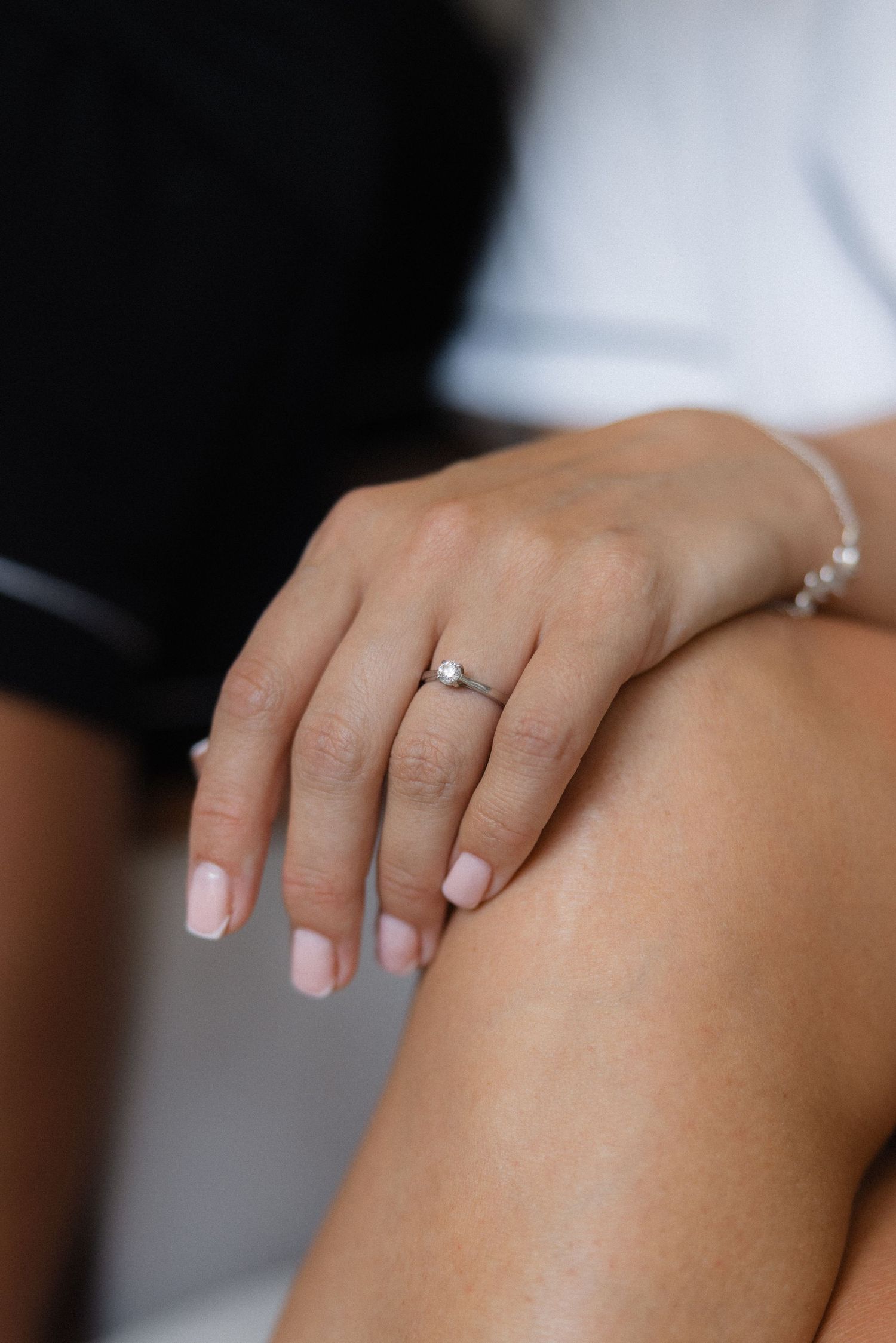 Close-up of manicured hands with engagement ring resting on knee.