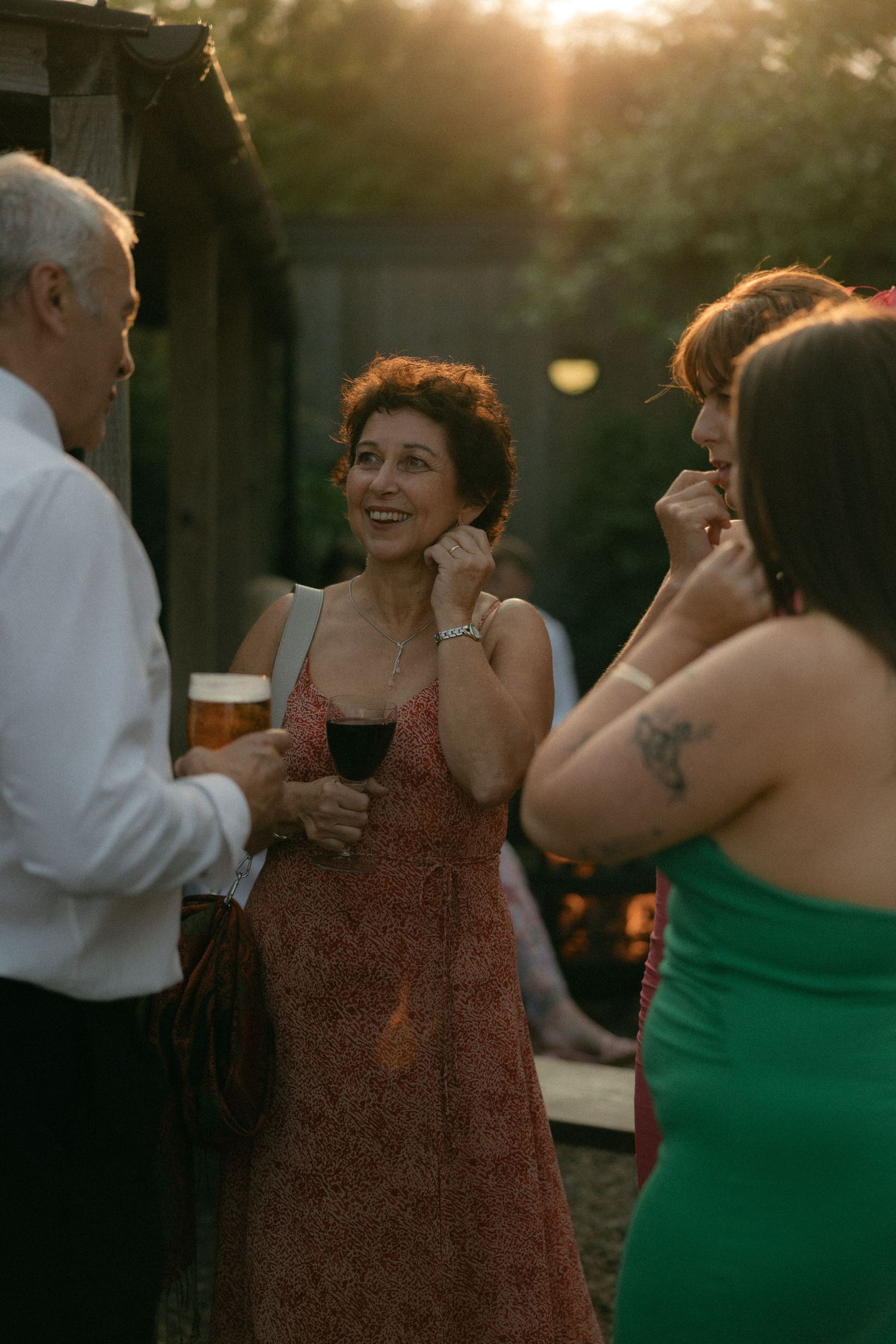 Wedding guests in colorful attire enjoying drinks and conversation at sunset.