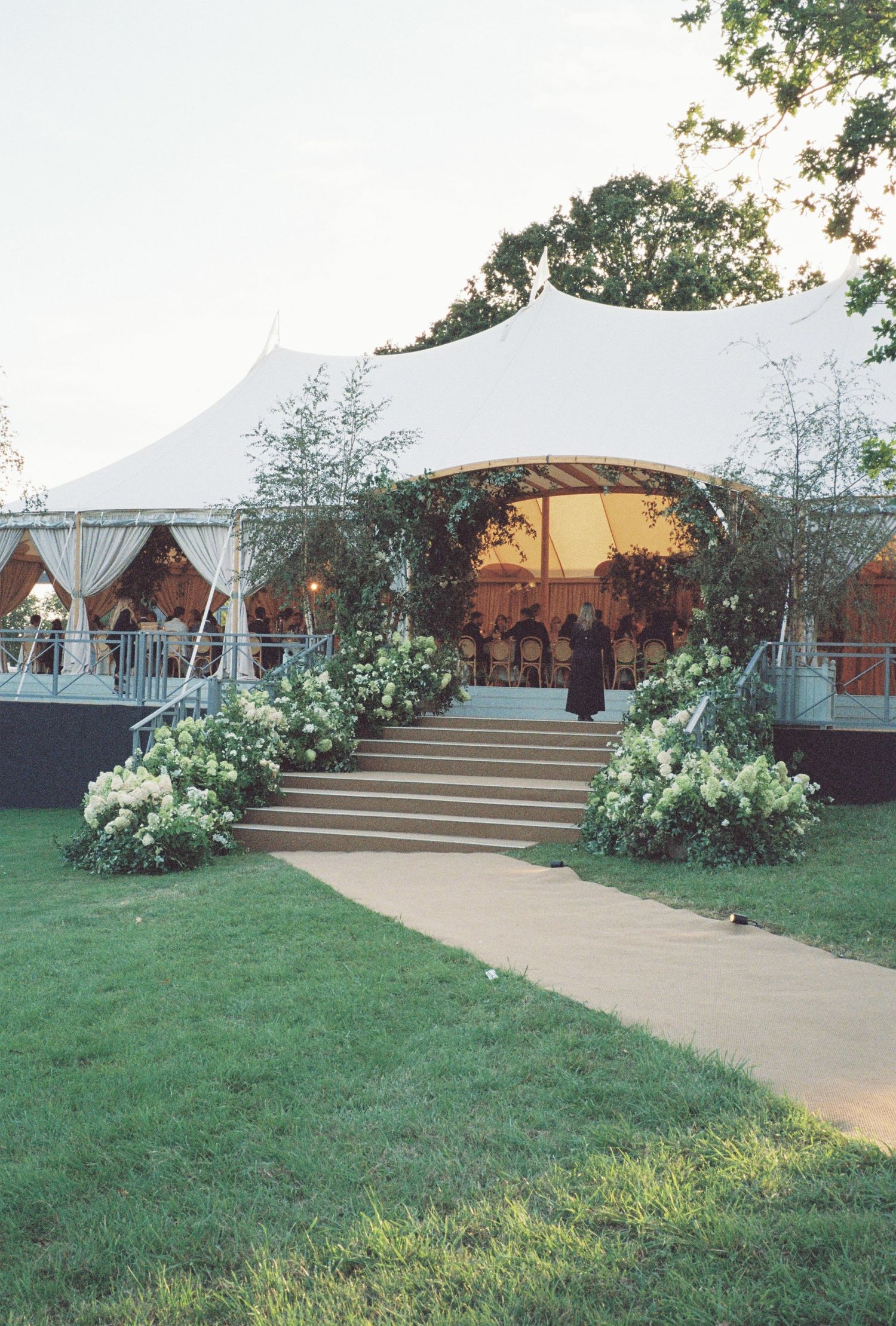 An elegant outdoor wedding tent setup with white canopy and floral decorations.