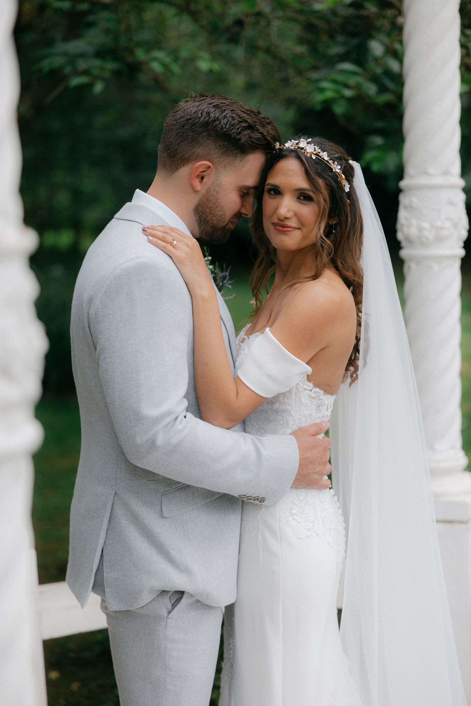 A romantic moment captured between newlyweds under white garden pillars.