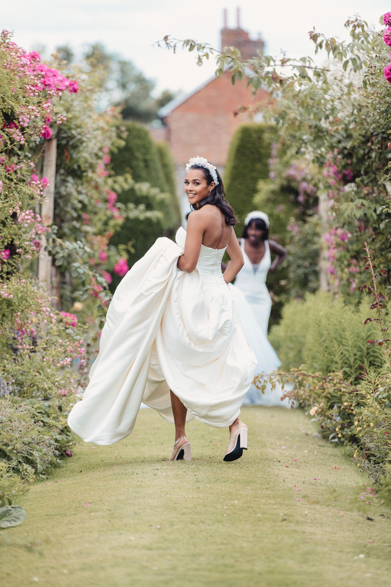 Playful bridal photos in a garden with pink flowers as bride lifts dress while walking.