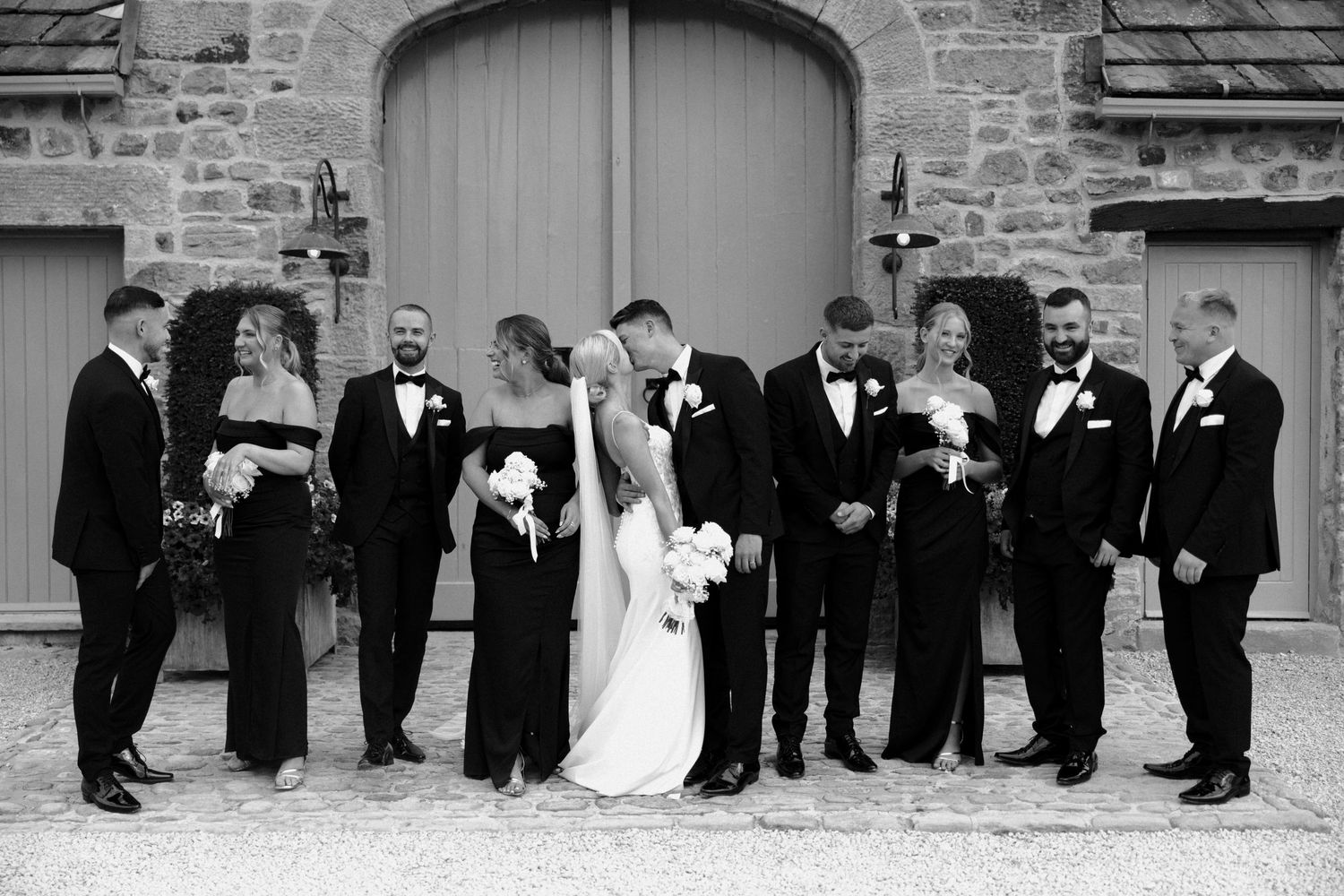 Wedding party lined up against stone church wall in formal attire.