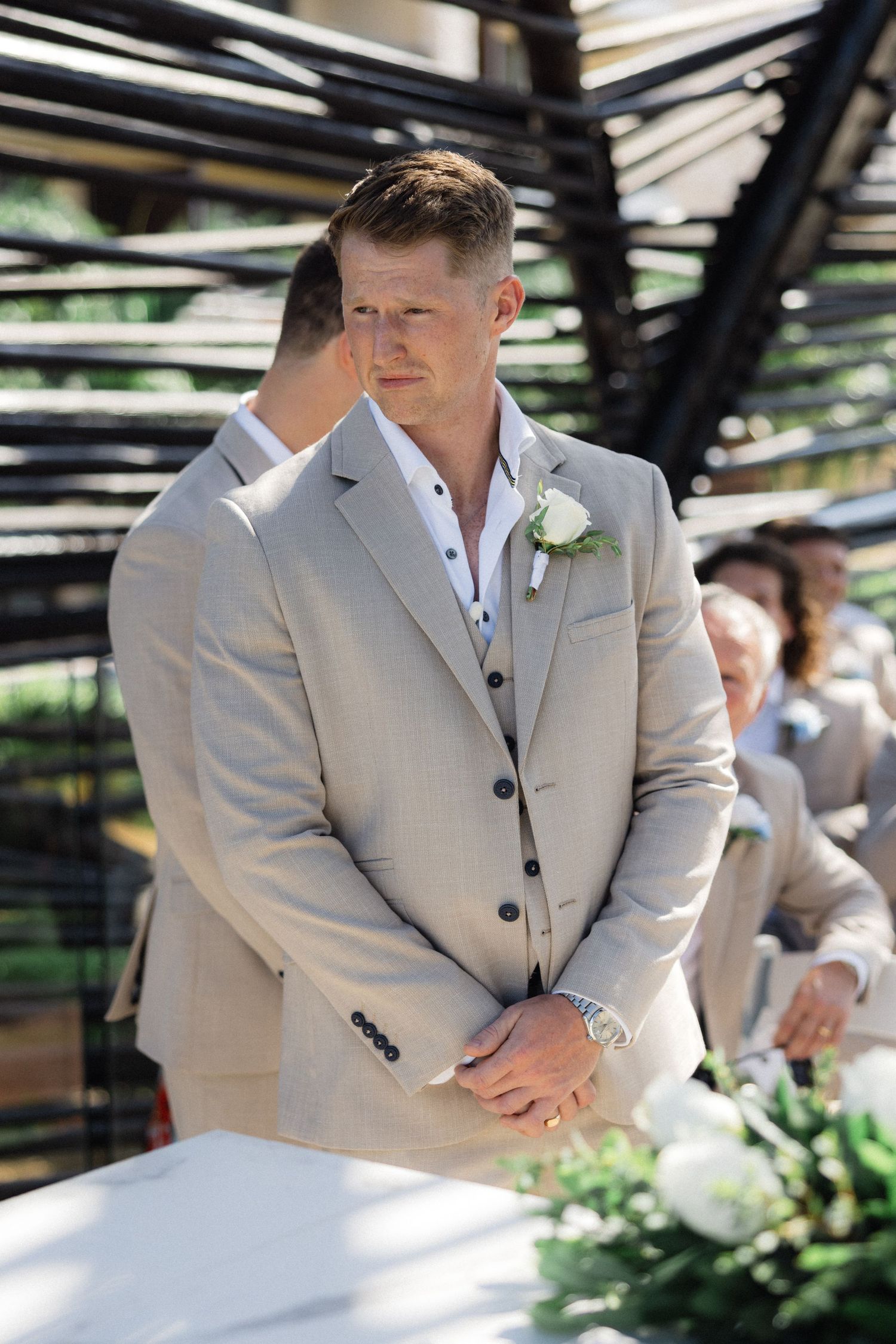 Groomsmen in light beige suits standing at attention during outdoor ceremony.