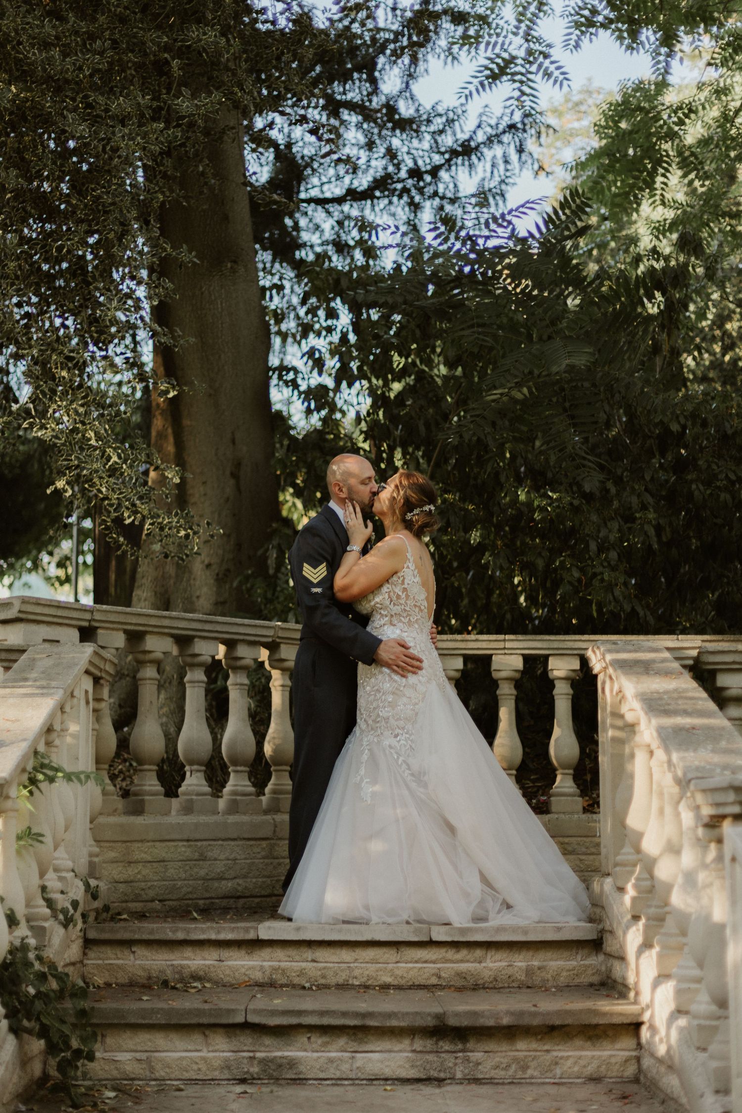 Romantic wedding portrait of couple embracing on elegant stone steps in garden setting.