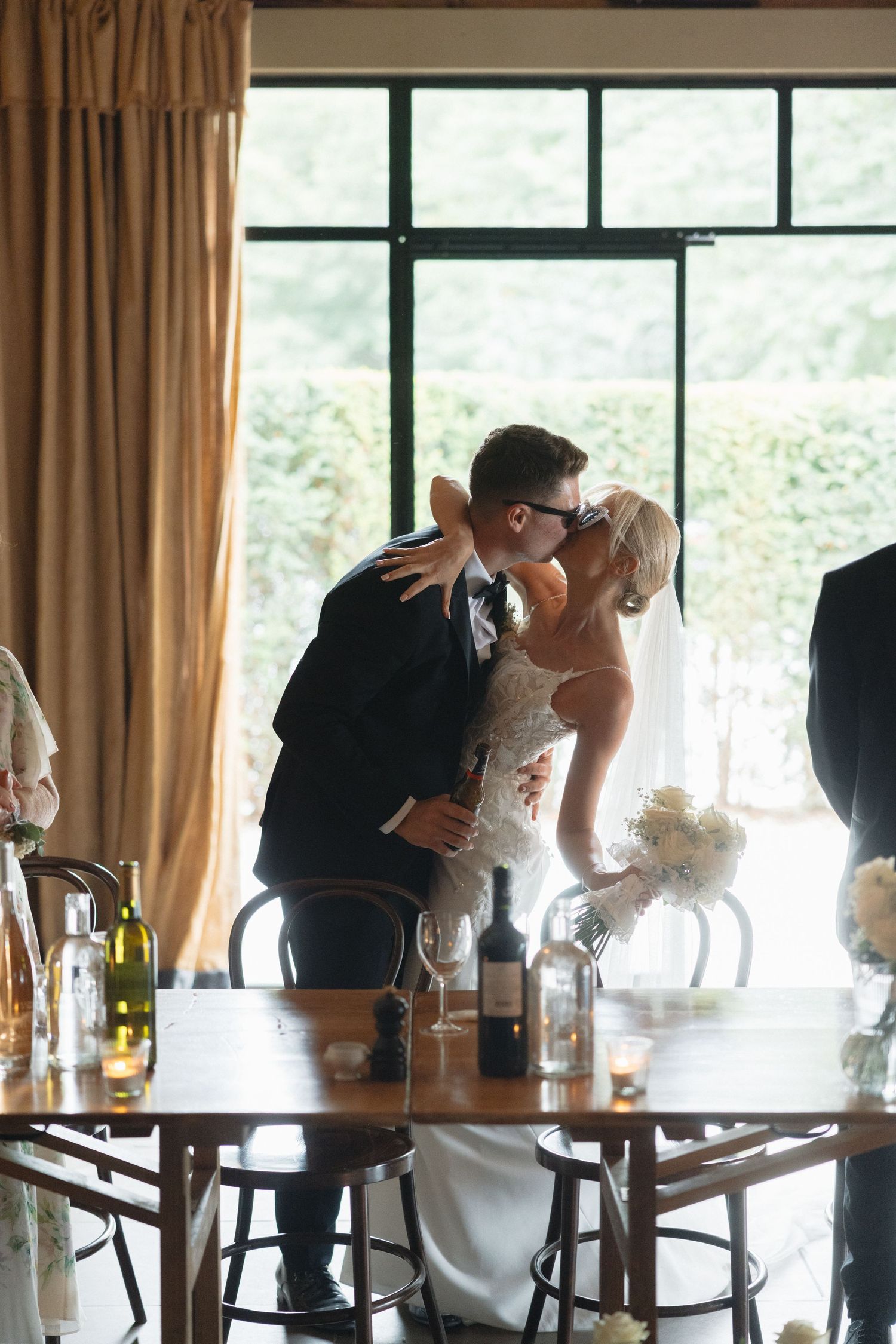 Wedding celebration in a sunlit room with large windows and elegant table settings.