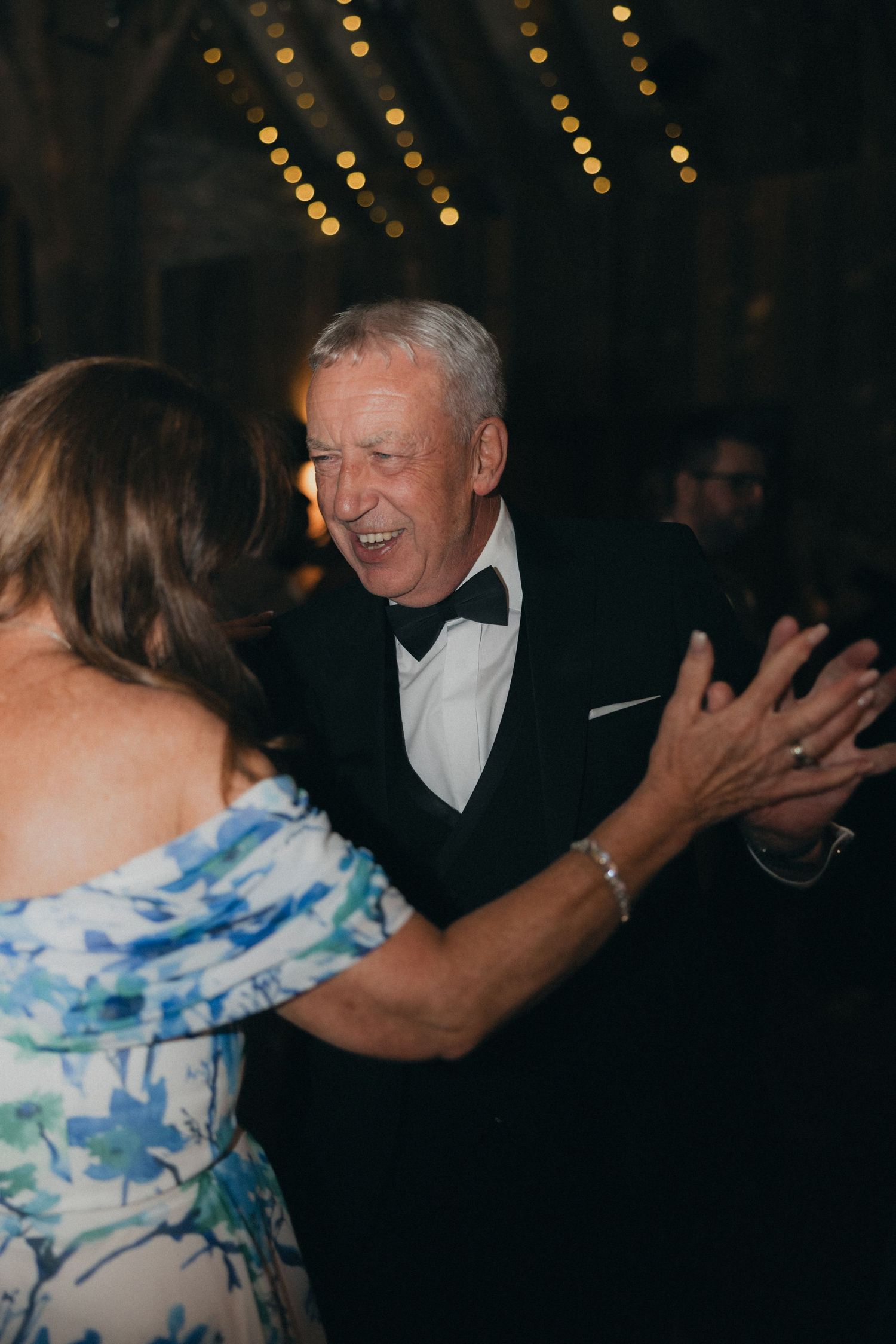 Guests share a joyful dance moment at an evening wedding reception under string lights.