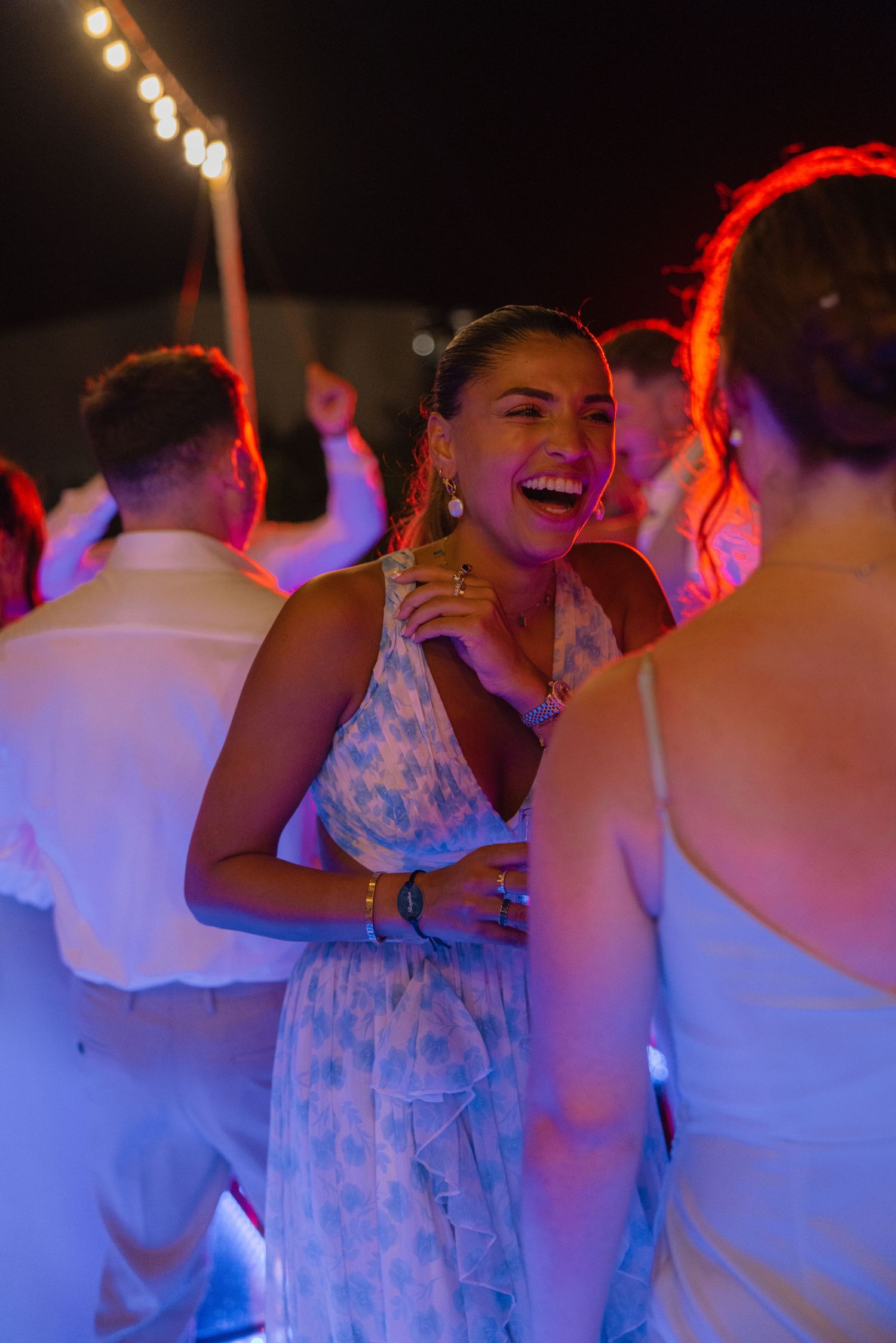 Wedding guests dancing and laughing under colorful party lights at night.
