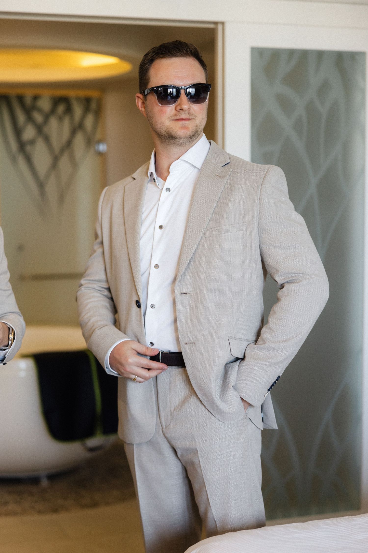 Person in light colored suit and sunglasses standing confidently in modern interior.