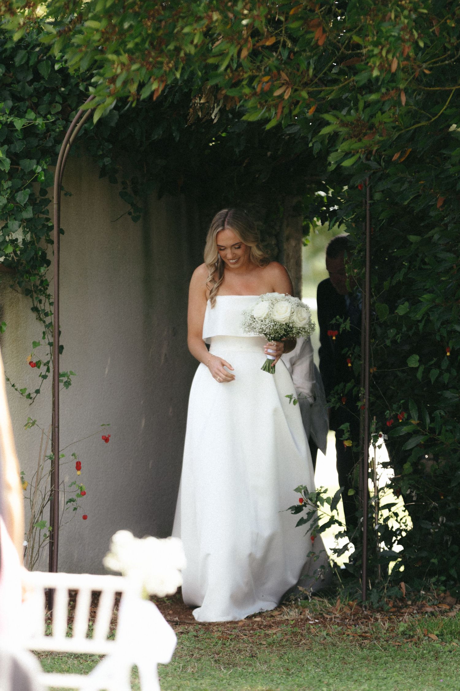 Wedding dress detail through garden greenery and white fence.