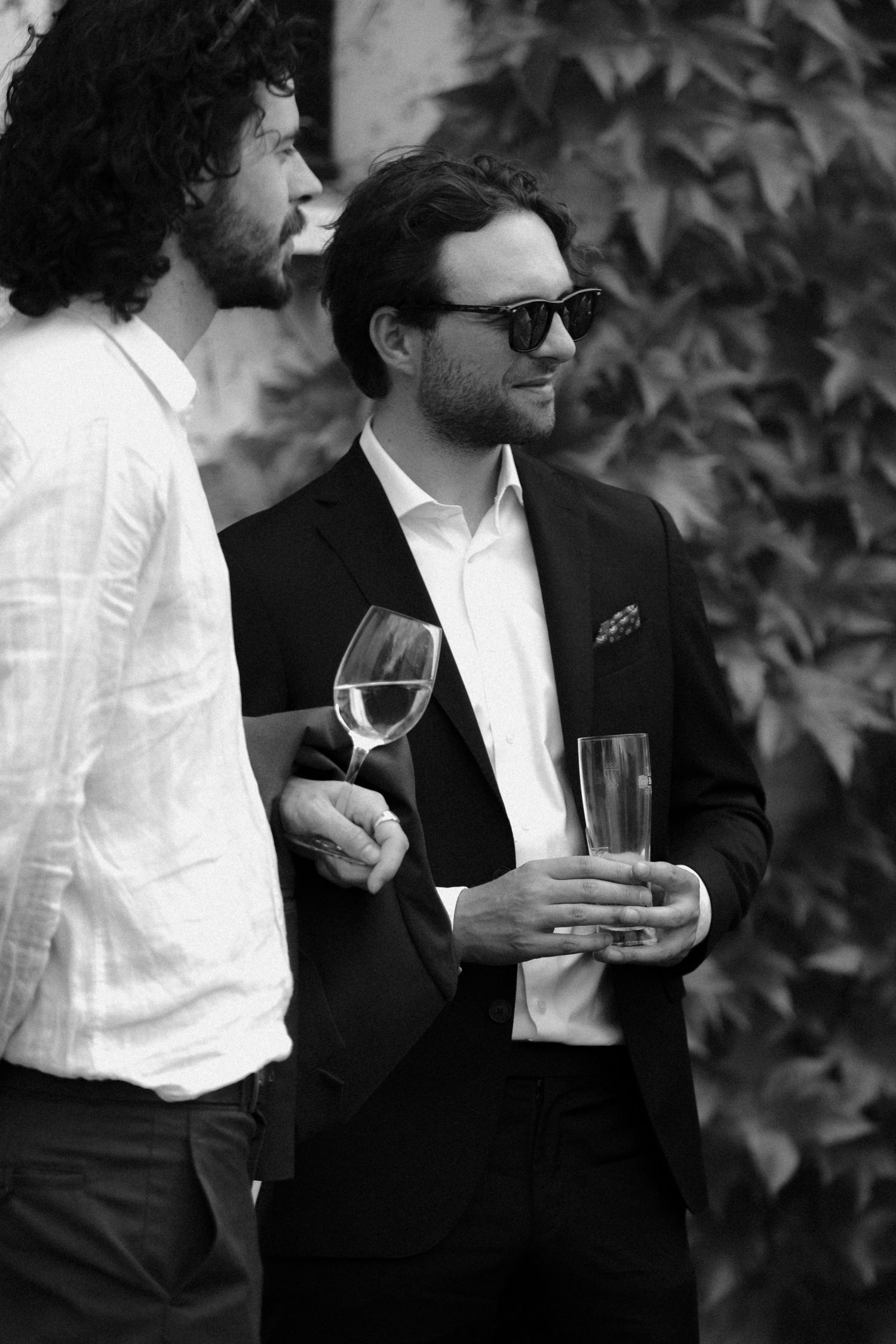 Two guests in formal attire hold wine glasses at outdoor event.