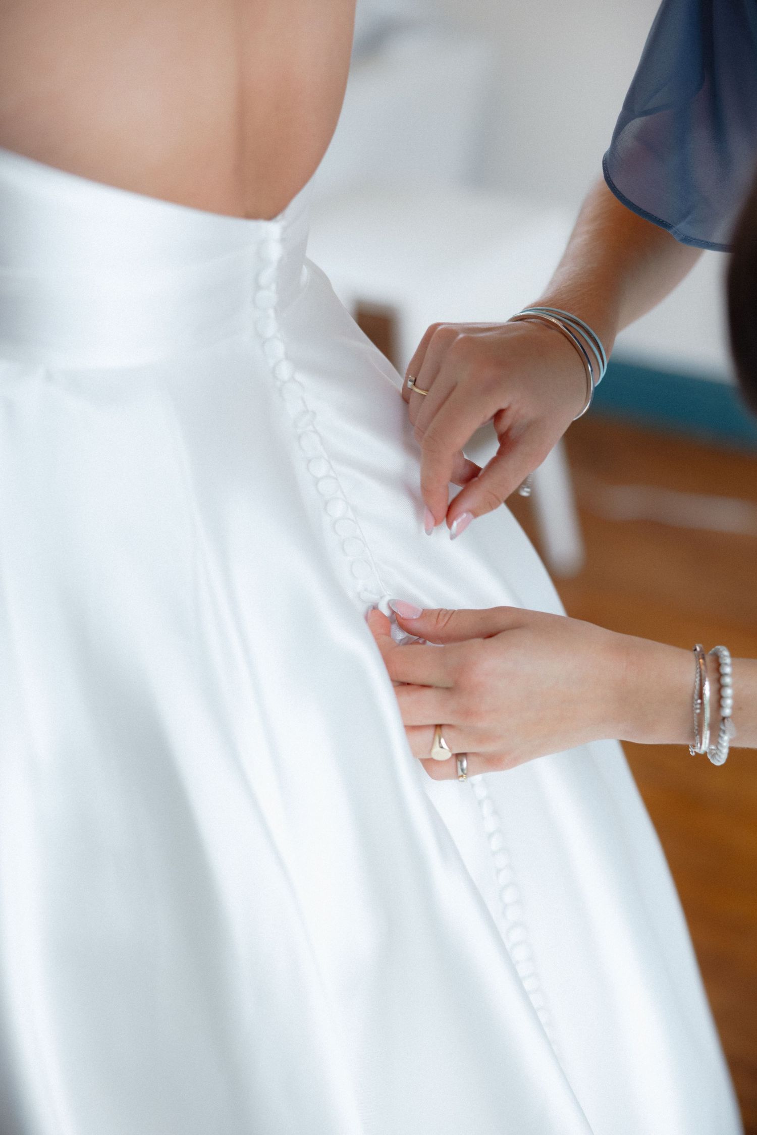 Close-up of hands adjusting buttons on white wedding dress.