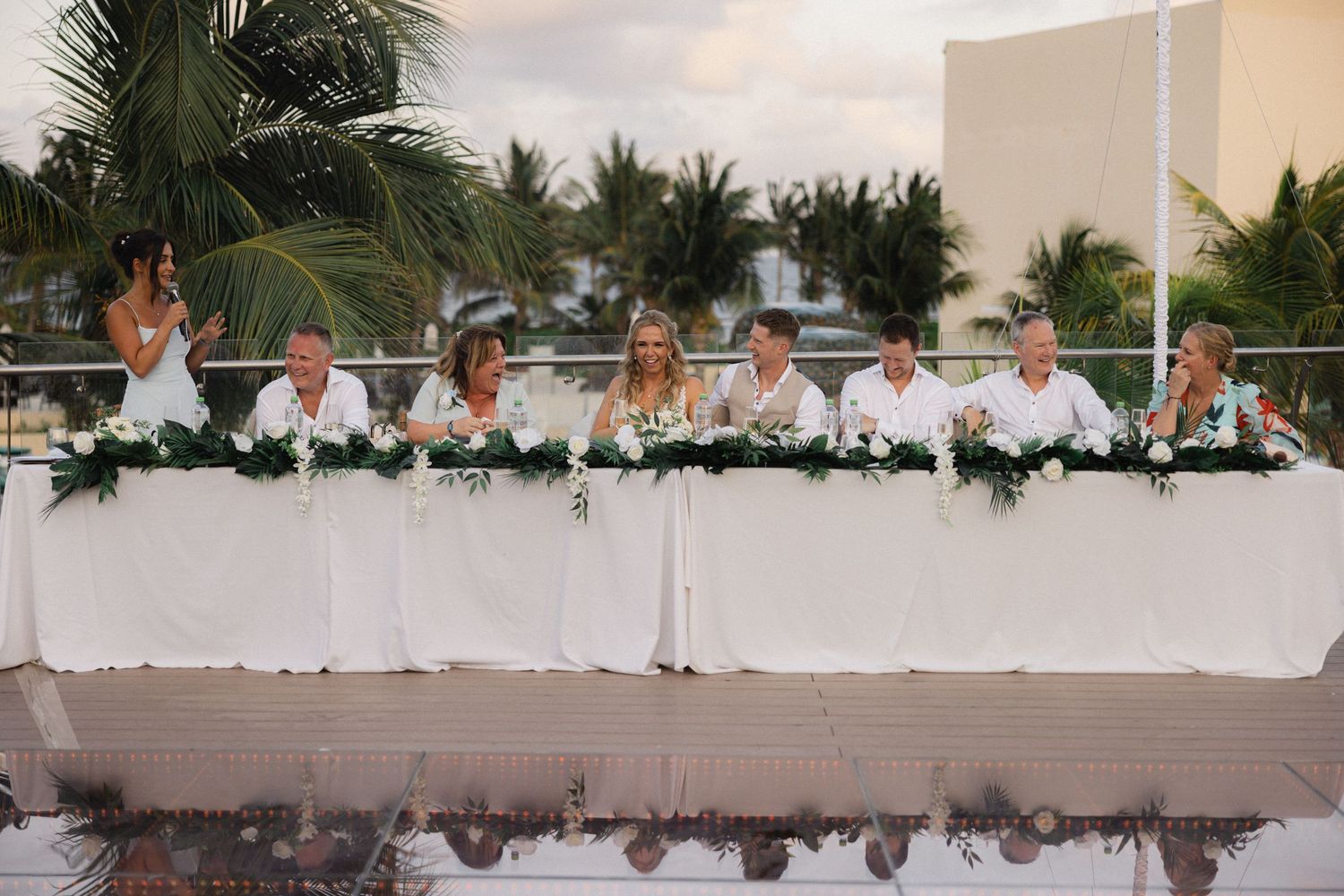 Panoramic view of wedding reception tables decorated in white against palm trees.