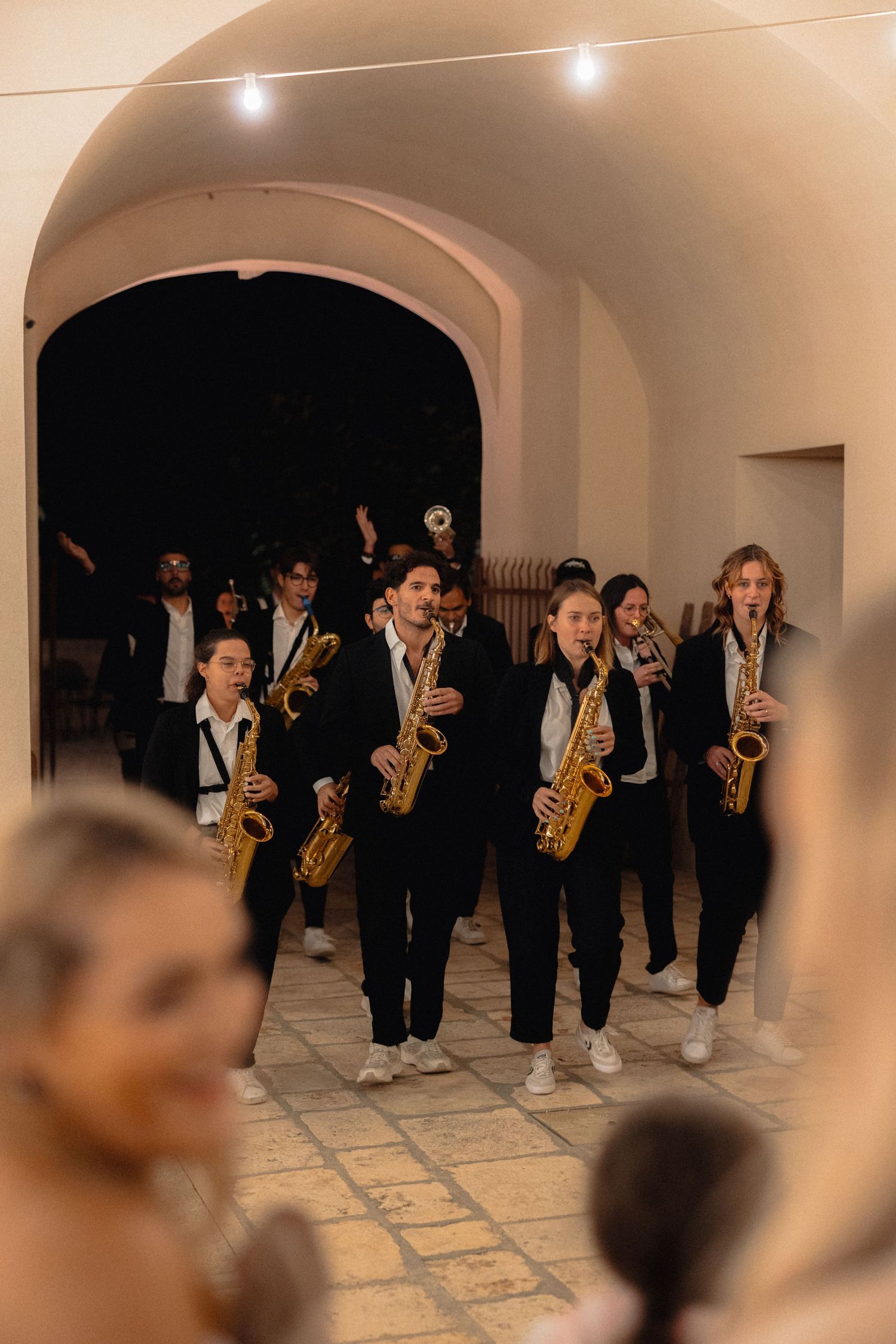 A saxophone band performs in formal attire under arched hallways with stone flooring.