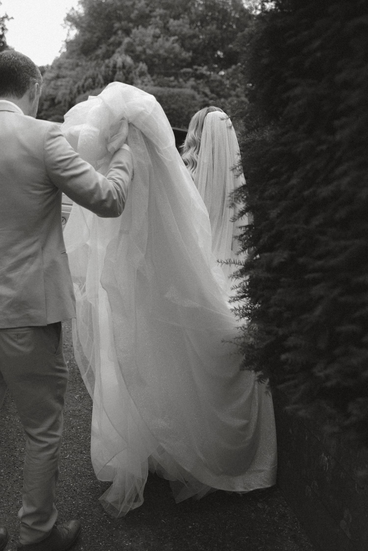 A couple in wedding attire playfully twirling in an outdoor garden setting.