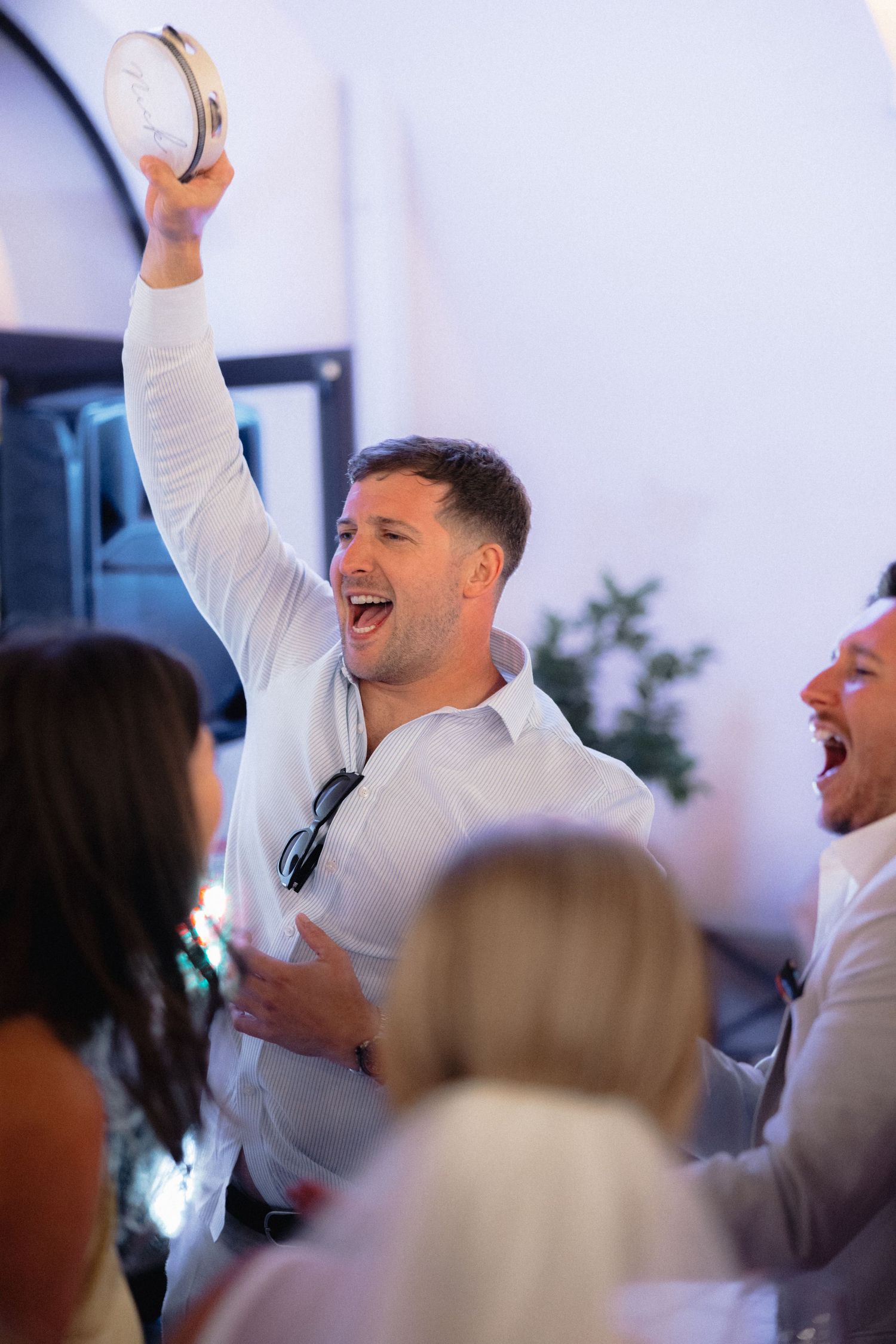 Joyful celebration at wedding reception with guests dancing and raising arms in excitement.