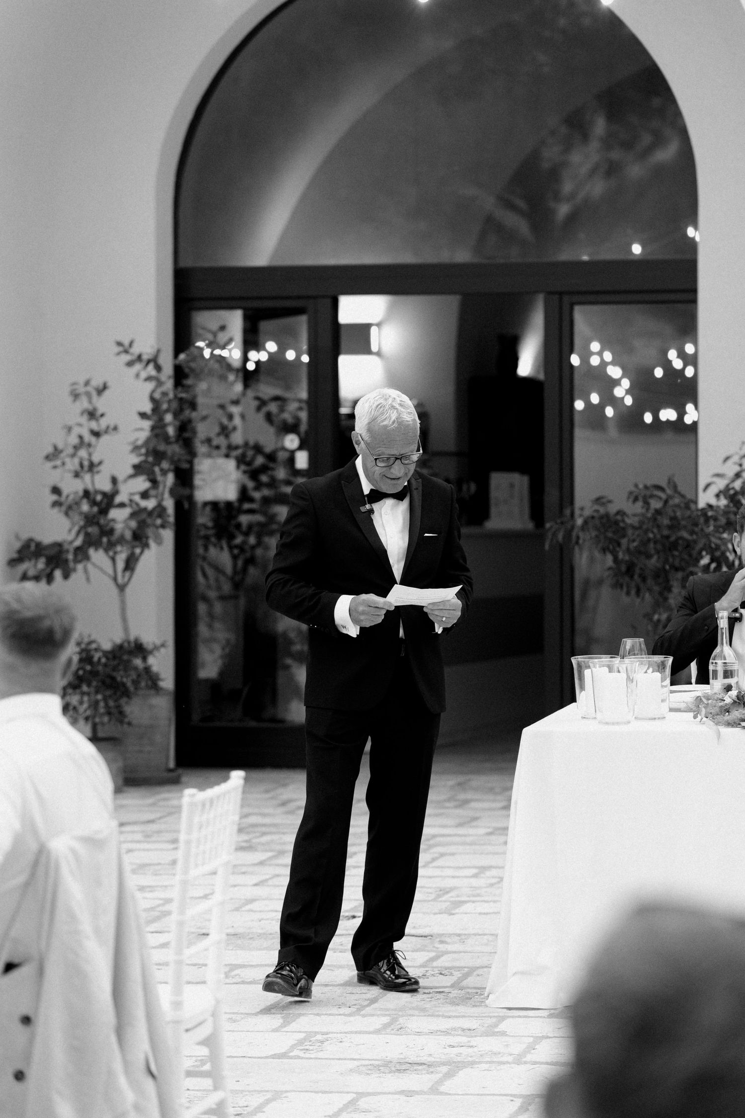 Black and white photo of wedding setup with white chairs and string lights.
